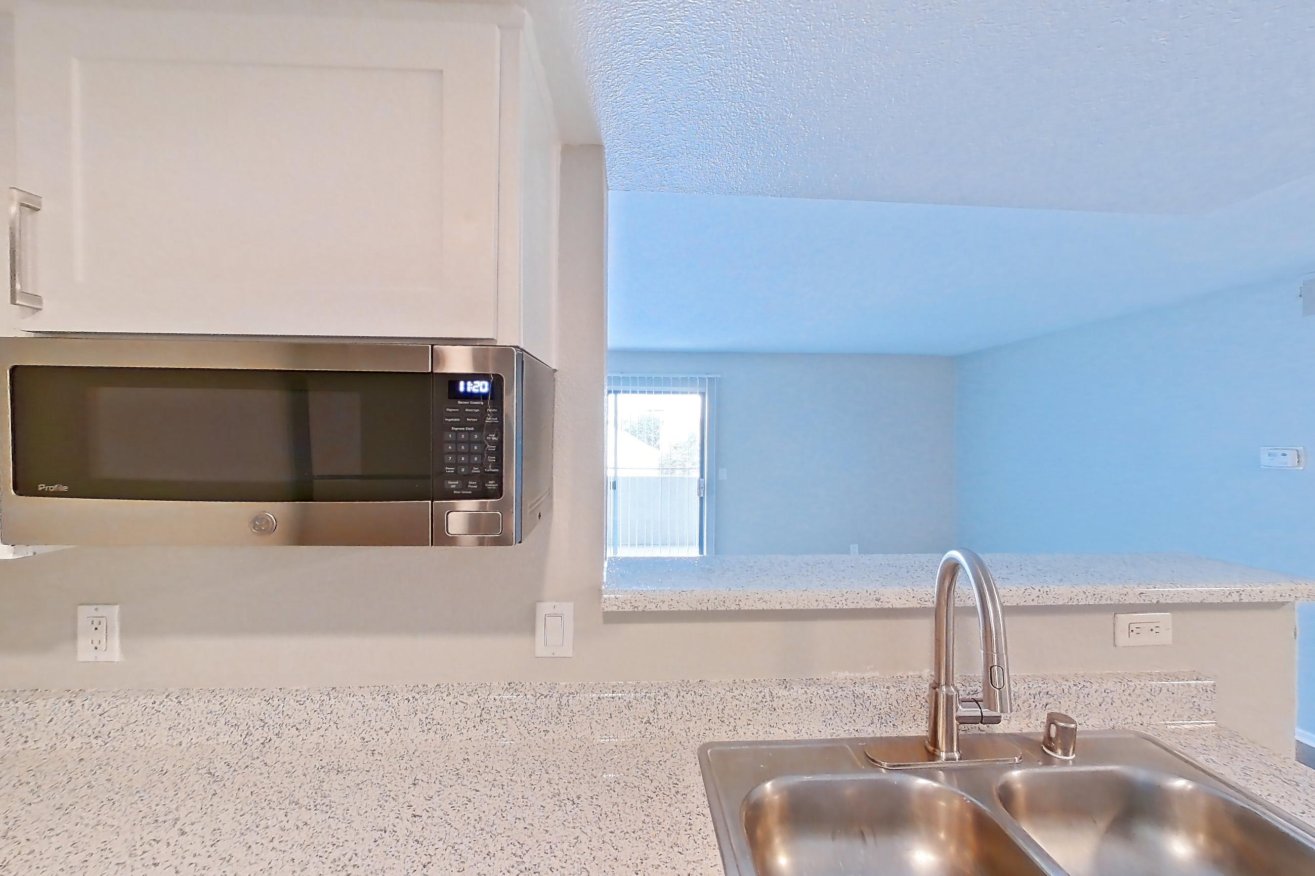 Kitchen with dishwasher, electric range, in-unit laundry, light countertops, light stone countertops, light wood-finish flooring, microwave, and stainless steel appliances, Apartment 21 at Avana Rancho Cucamonga