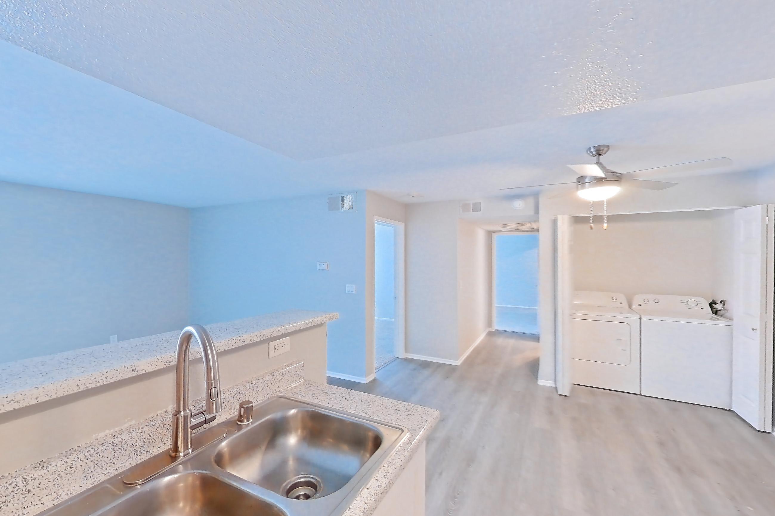 Kitchen with dishwasher, electric range, in-unit laundry, light countertops, light stone countertops, light wood-finish flooring, microwave, and stainless steel appliances, Apartment 21 at Avana Rancho Cucamonga