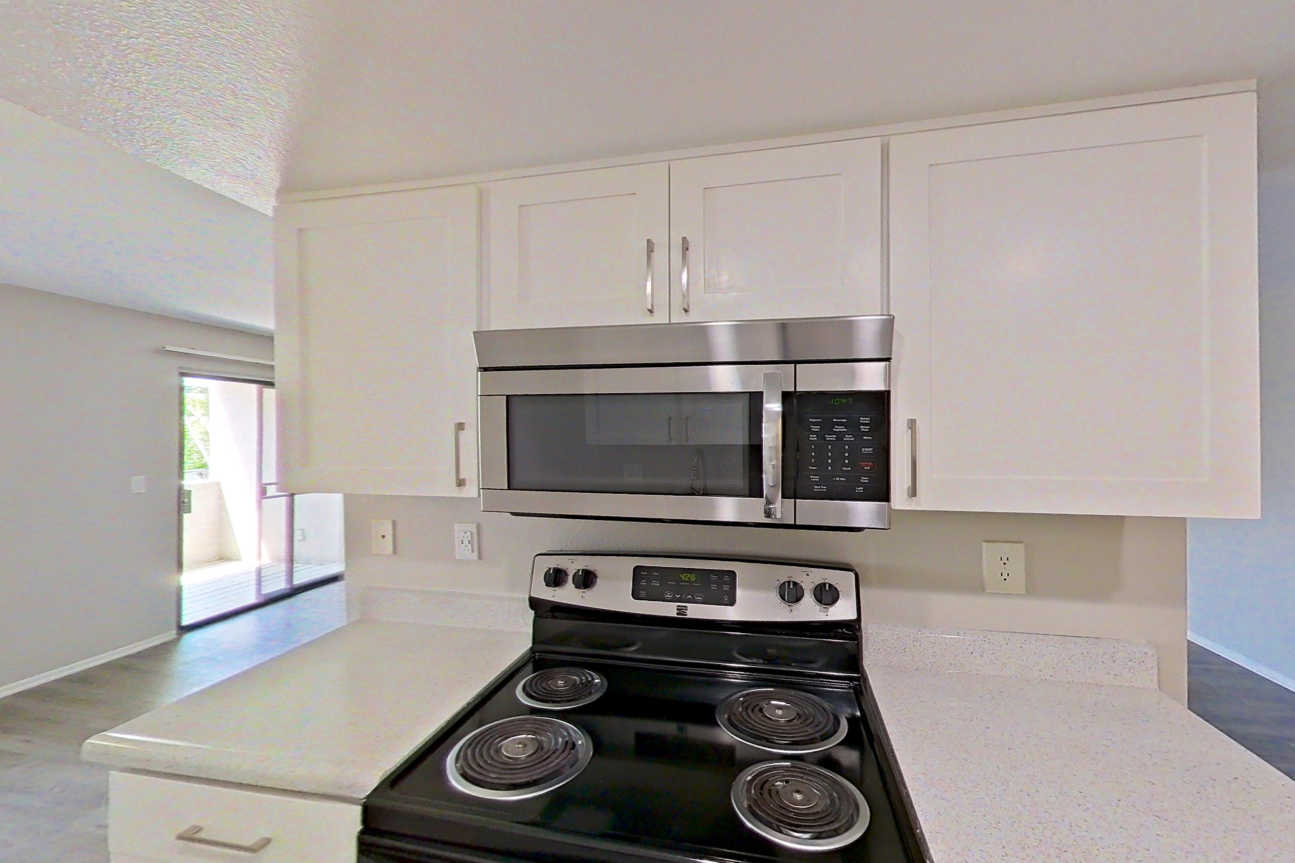 Kitchen with dishwasher, electric range, light countertops, light wood-finish flooring, microwave, oven/range, refrigerator, and stainless steel appliances, Apartment 07 at Avana Rancho Cucamonga