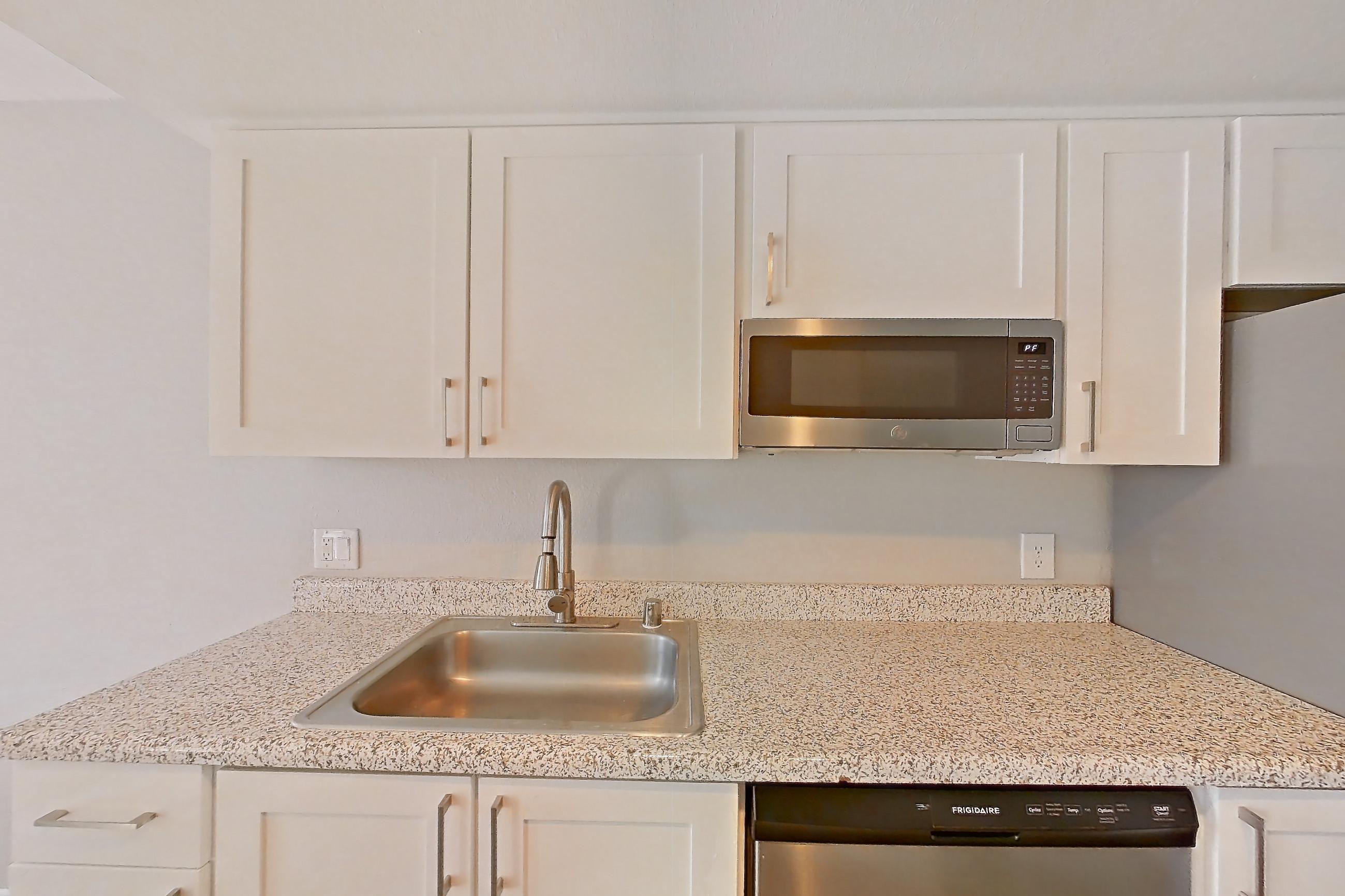 Kitchen with dishwasher, electric range, kitchen island, light stone countertops, light wood-finish flooring, oven/range, range hood, refrigerator, and stainless steel appliances, Apartment 09 at Avana Rancho Cucamonga