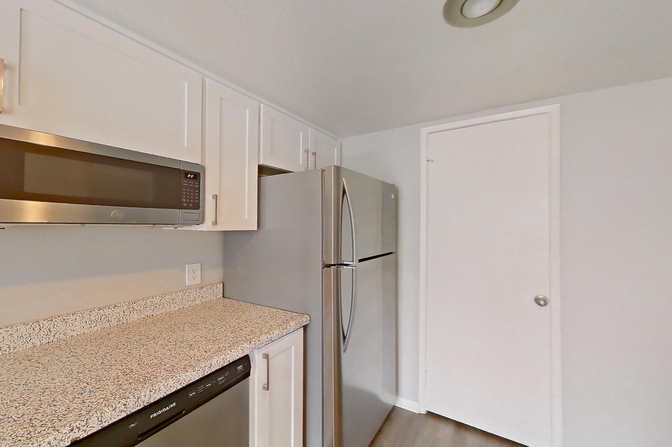Kitchen with dishwasher, electric range, kitchen island, light stone countertops, light wood-finish flooring, oven/range, range hood, refrigerator, and stainless steel appliances, Apartment 09 at Avana Rancho Cucamonga