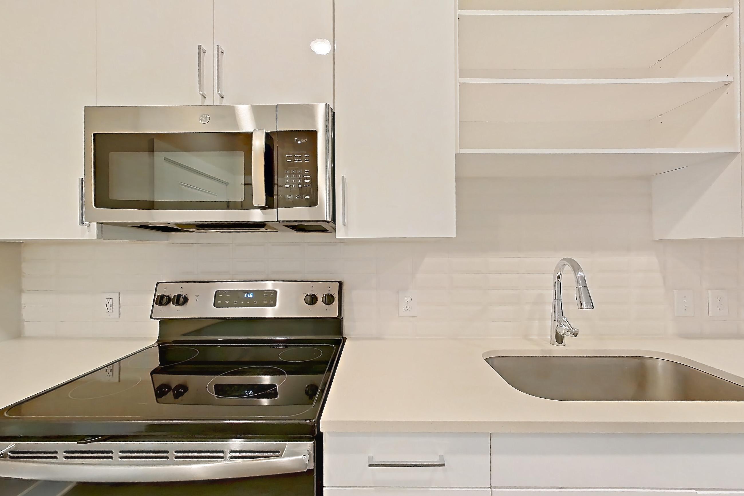 Kitchen with dark wood-finish flooring, dishwasher, electric range, light countertops, microwave, oven/range, refrigerator, and stainless steel appliances, Apartment 1278 at Cortland at the Hill