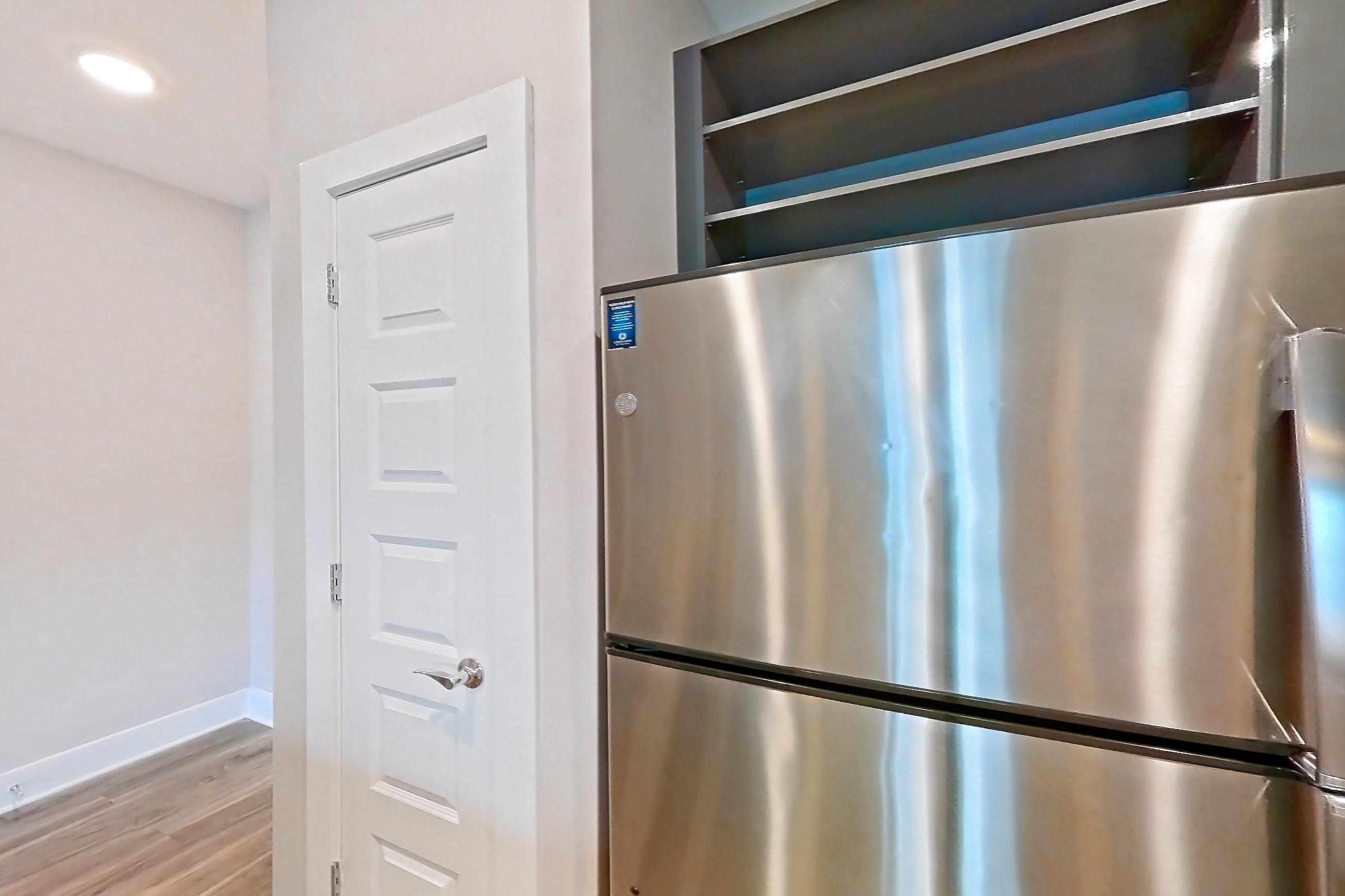 Kitchen with dishwasher, electric range, kitchen island, light countertops, light stone countertops, light wood-finish flooring, microwave, oven/range, refrigerator, and stainless steel appliances, Apartment 1544 at Cortland at the Hill