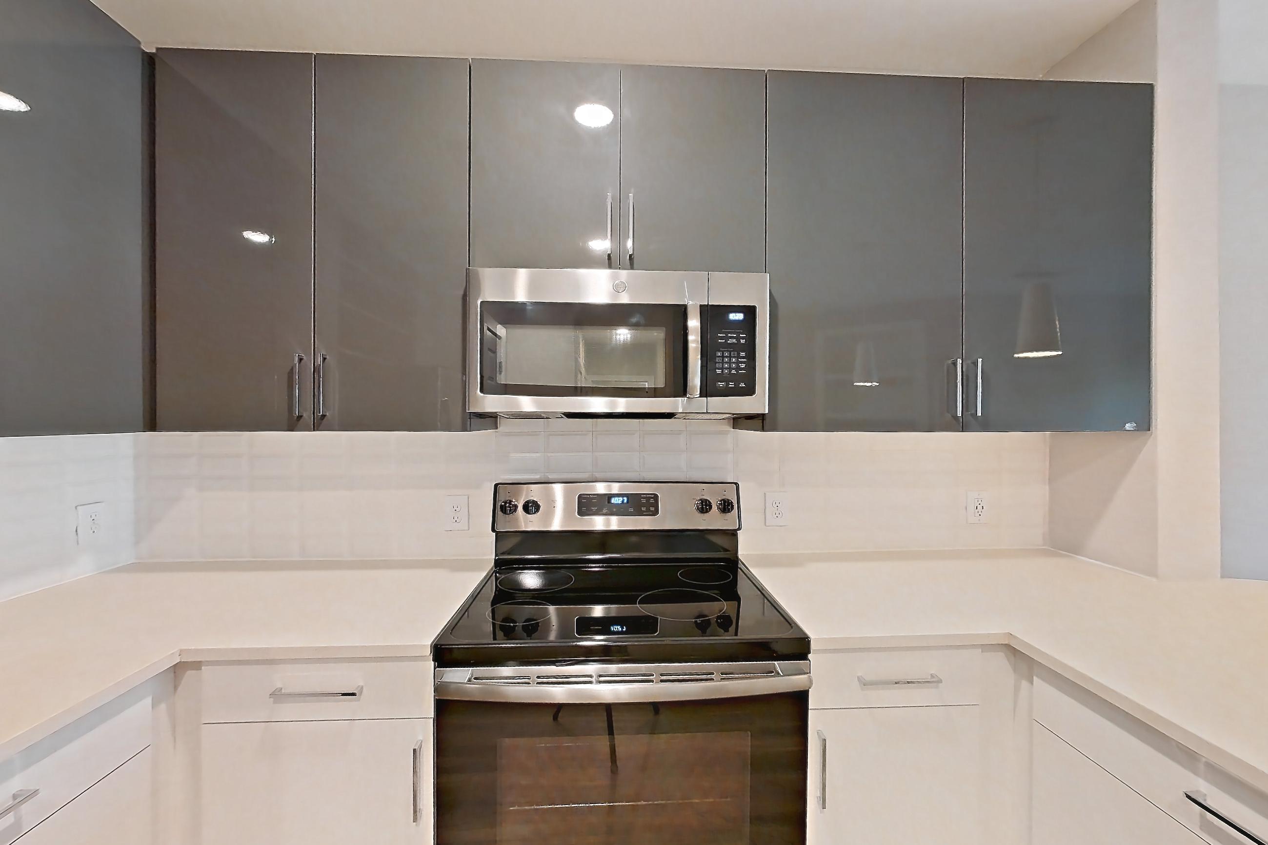 Kitchen with dishwasher, electric range, kitchen island, light countertops, light stone countertops, light wood-finish flooring, microwave, oven/range, refrigerator, and stainless steel appliances, Apartment 1544 at Cortland at the Hill