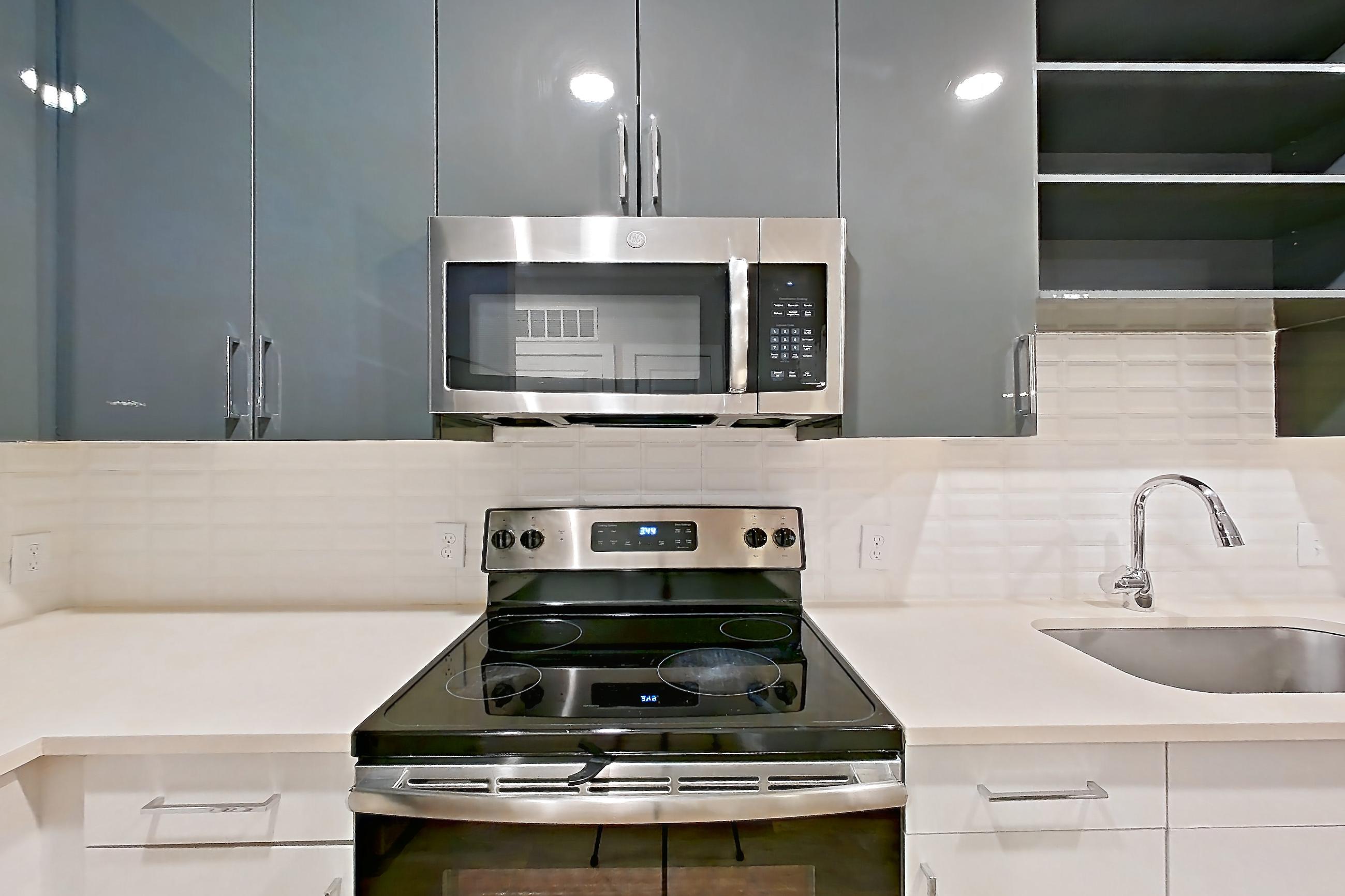 Kitchen with dishwasher, electric range, light countertops, light stone countertops, light wood-finish flooring, microwave, oven/range, refrigerator, and stainless steel appliances, Apartment 1080 at Cortland at the Hill