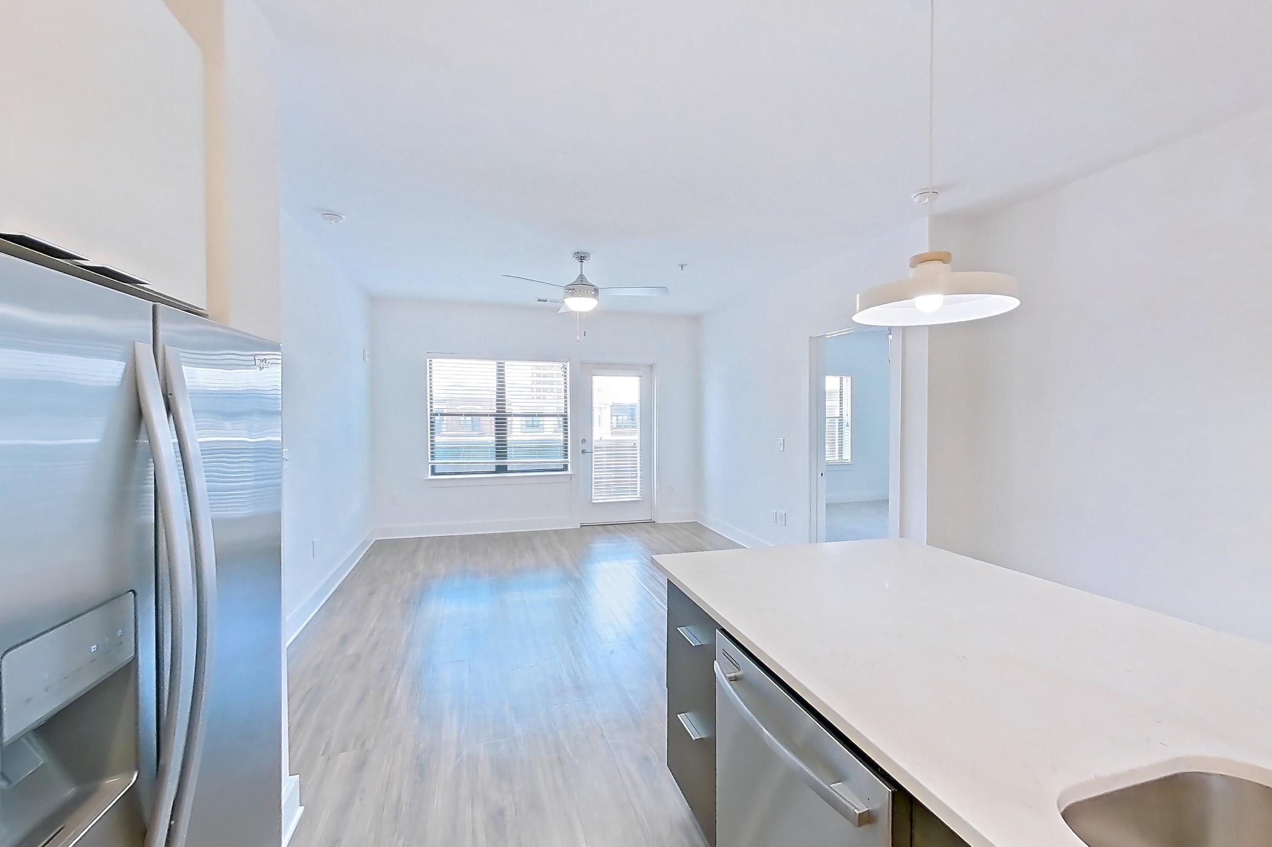 Kitchen with dishwasher, light countertops, light stone countertops, light wood-finish flooring, oven/range, refrigerator, stainless steel appliances, and water & ice dispenser, Apartment 613 at Cortland at the Battery