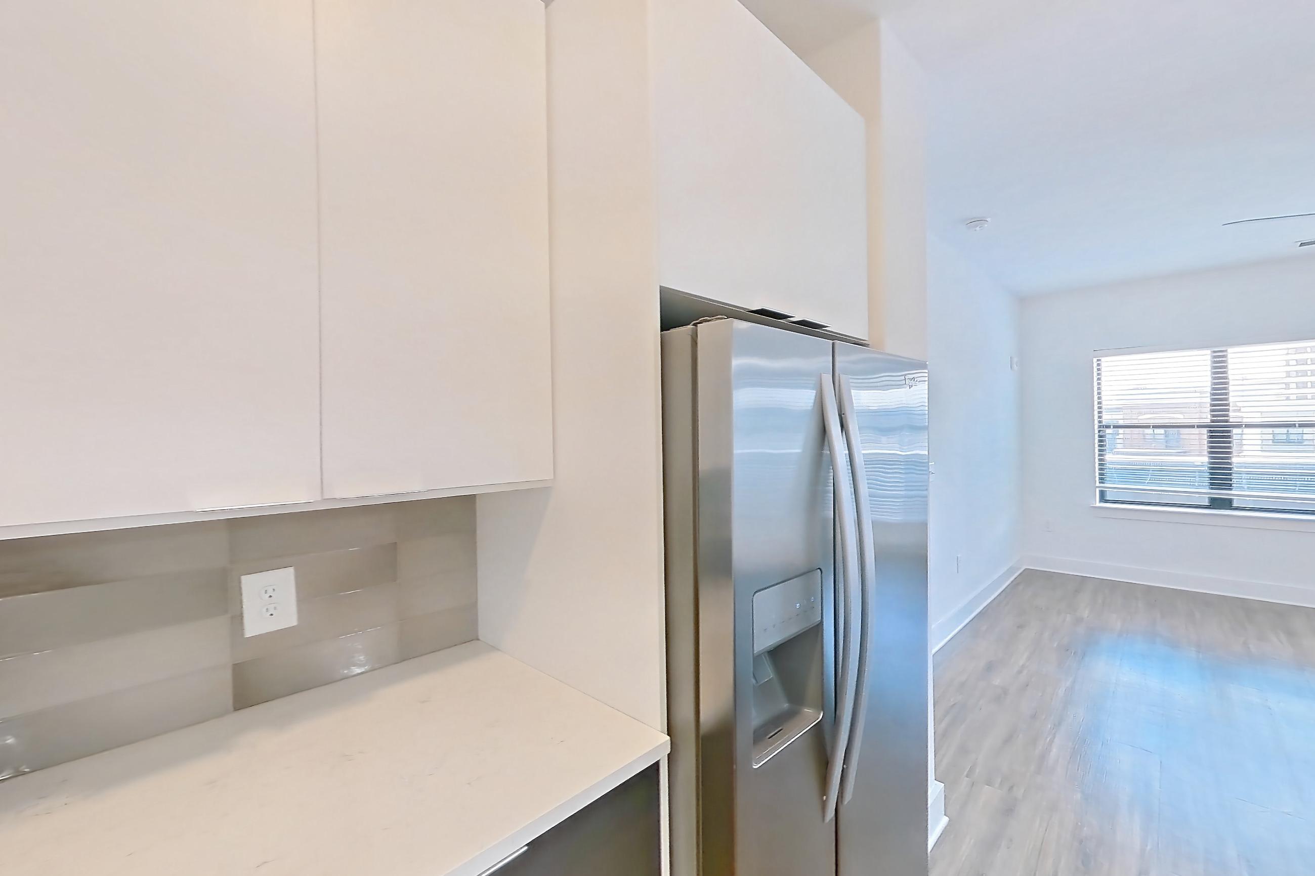 Kitchen with dishwasher, light countertops, light stone countertops, light wood-finish flooring, oven/range, refrigerator, stainless steel appliances, and water & ice dispenser, Apartment 613 at Cortland at the Battery