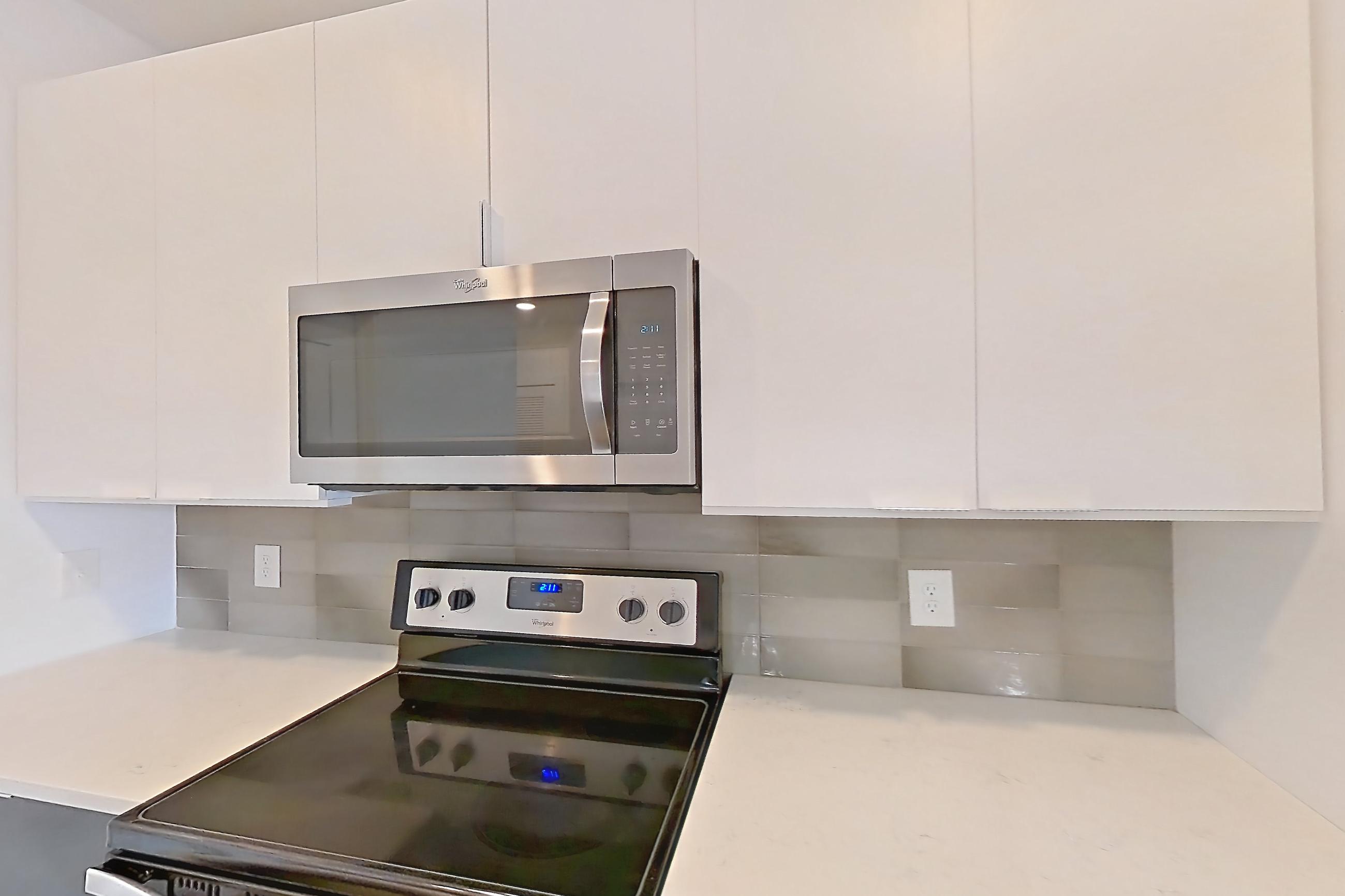 Kitchen with dishwasher, light countertops, light stone countertops, light wood-finish flooring, oven/range, refrigerator, stainless steel appliances, and water & ice dispenser, Apartment 613 at Cortland at the Battery