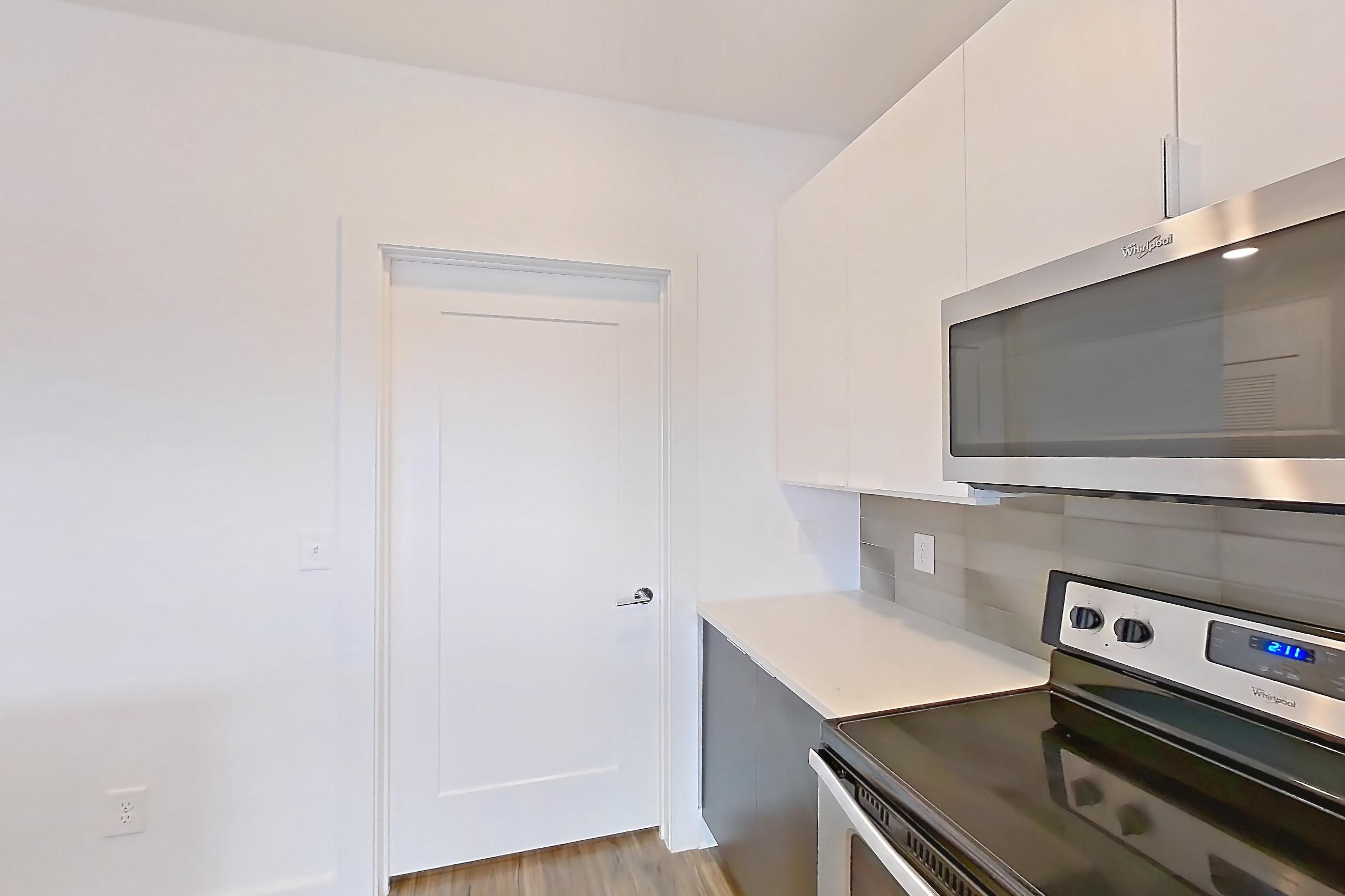 Kitchen with dishwasher, light countertops, light stone countertops, light wood-finish flooring, oven/range, refrigerator, stainless steel appliances, and water & ice dispenser, Apartment 613 at Cortland at the Battery