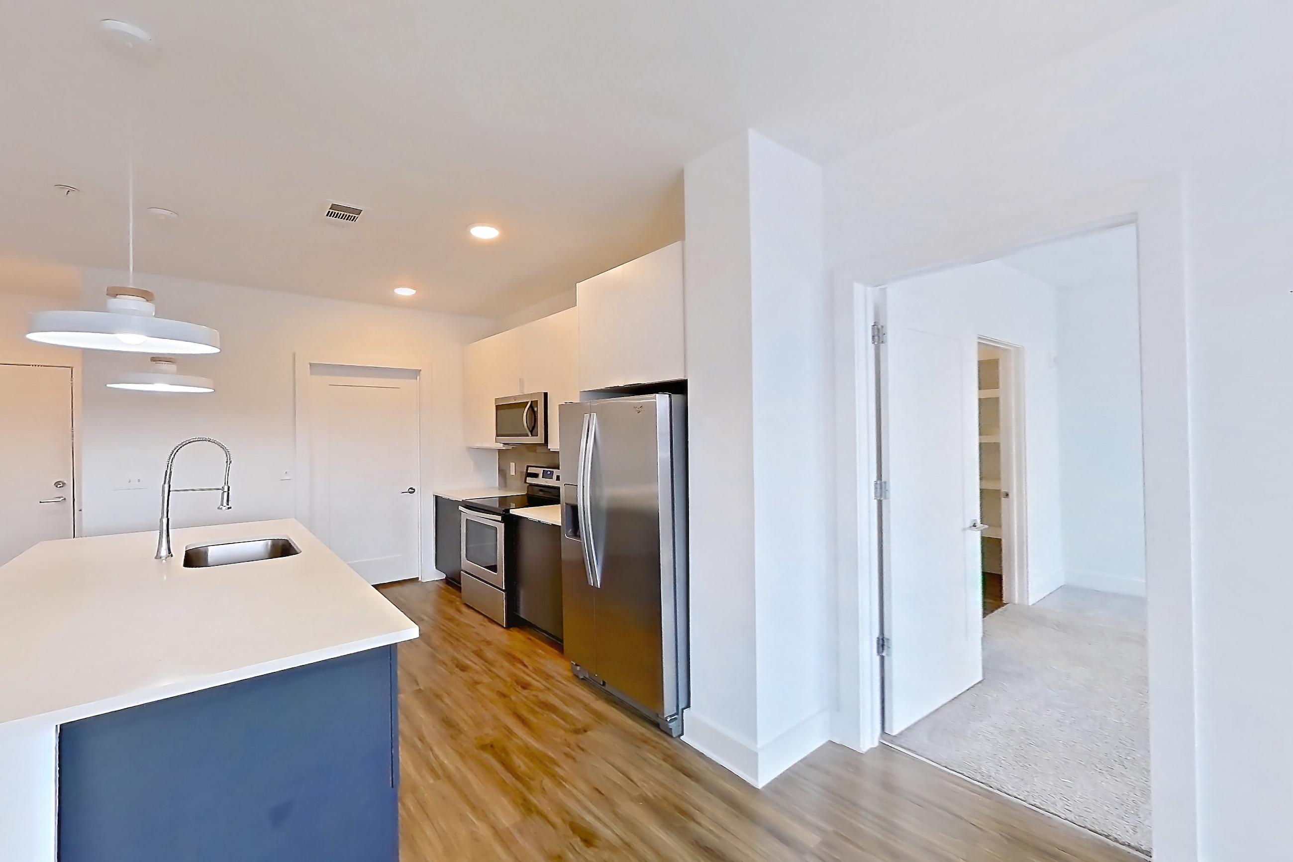 Living room with dark wood-finish flooring, oven/range, refrigerator, stainless steel appliances, and water & ice dispenser, Apartment 613 at Cortland at the Battery