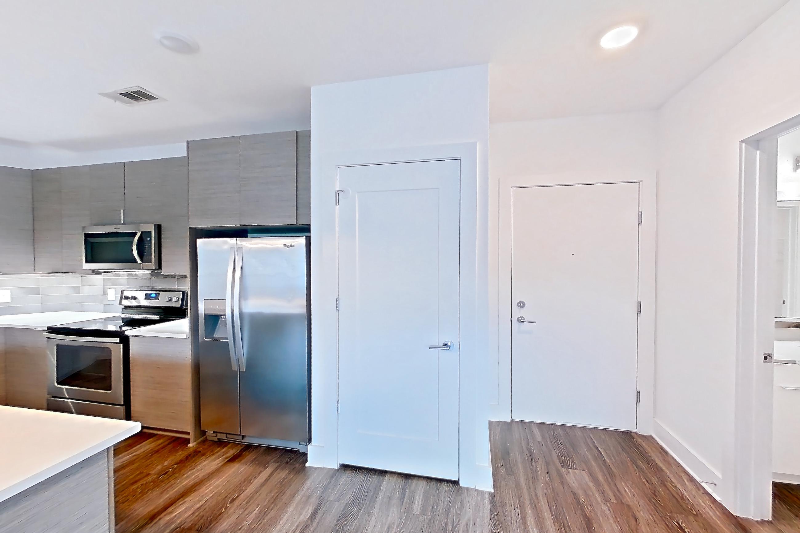 Living space with dark wood-finish flooring, electric range, kitchen island, light countertops, light stone countertops, oven/range, refrigerator, stainless steel appliances, and water & ice dispenser, Apartment 538 at Cortland at the Battery