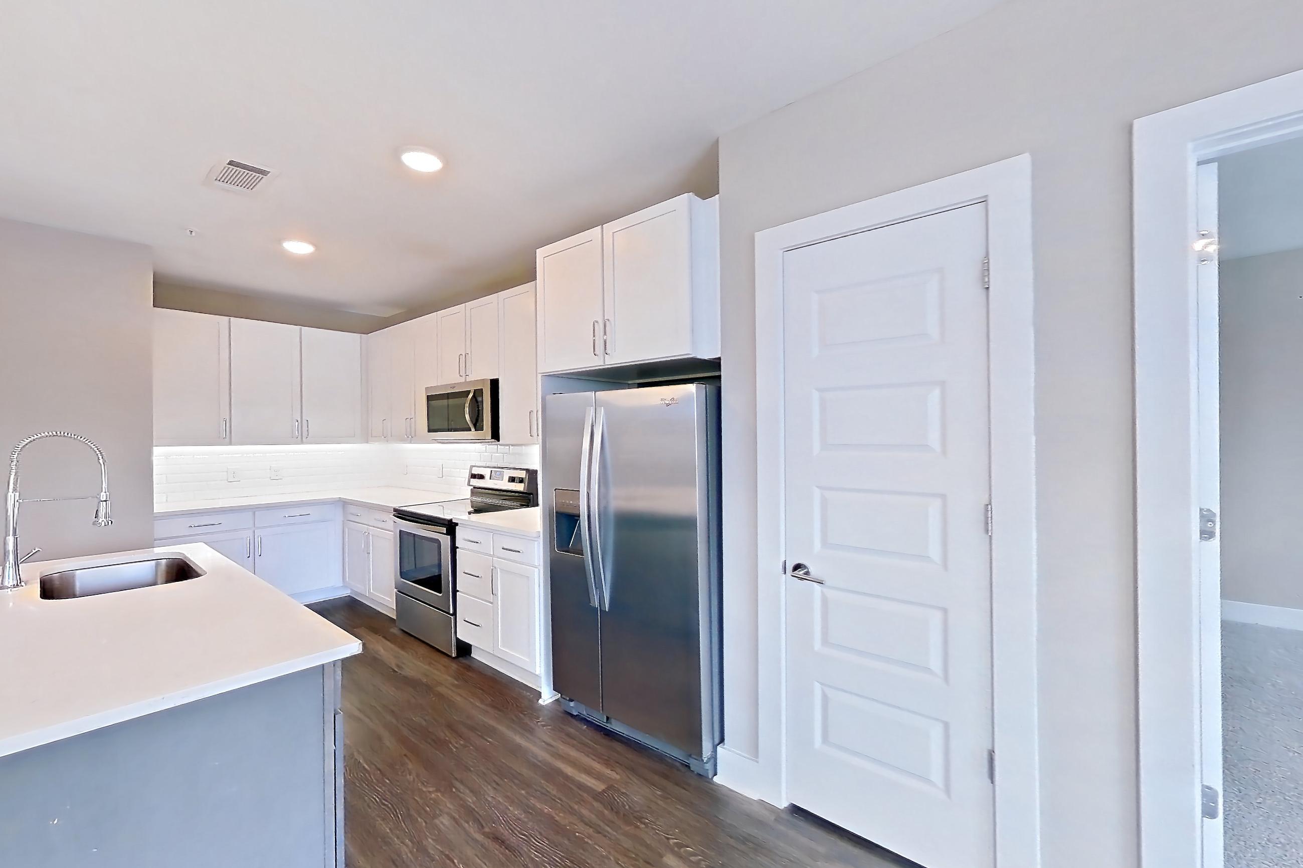 Living space with dark wood-finish flooring, light countertops, refrigerator, stainless steel appliances, and water & ice dispenser, Apartment 439 at Cortland at the Battery