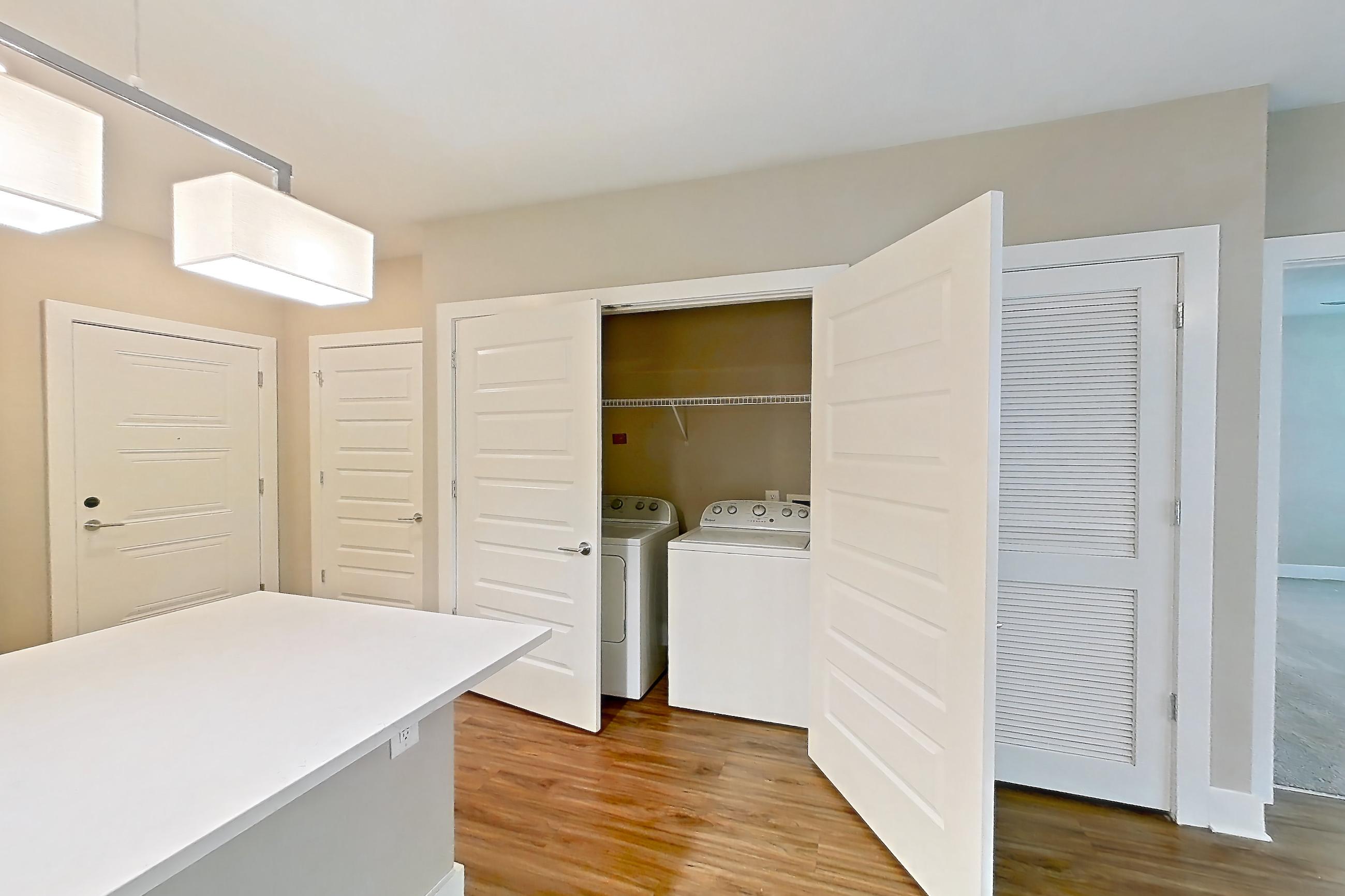 Dining room with dark wood-finish flooring, electric range, in-unit laundry, kitchen island, light countertops, light stone countertops, microwave, oven/range, refrigerator, stainless steel appliances, and water & ice dispenser, Apartment 307 at Cortland at the Battery