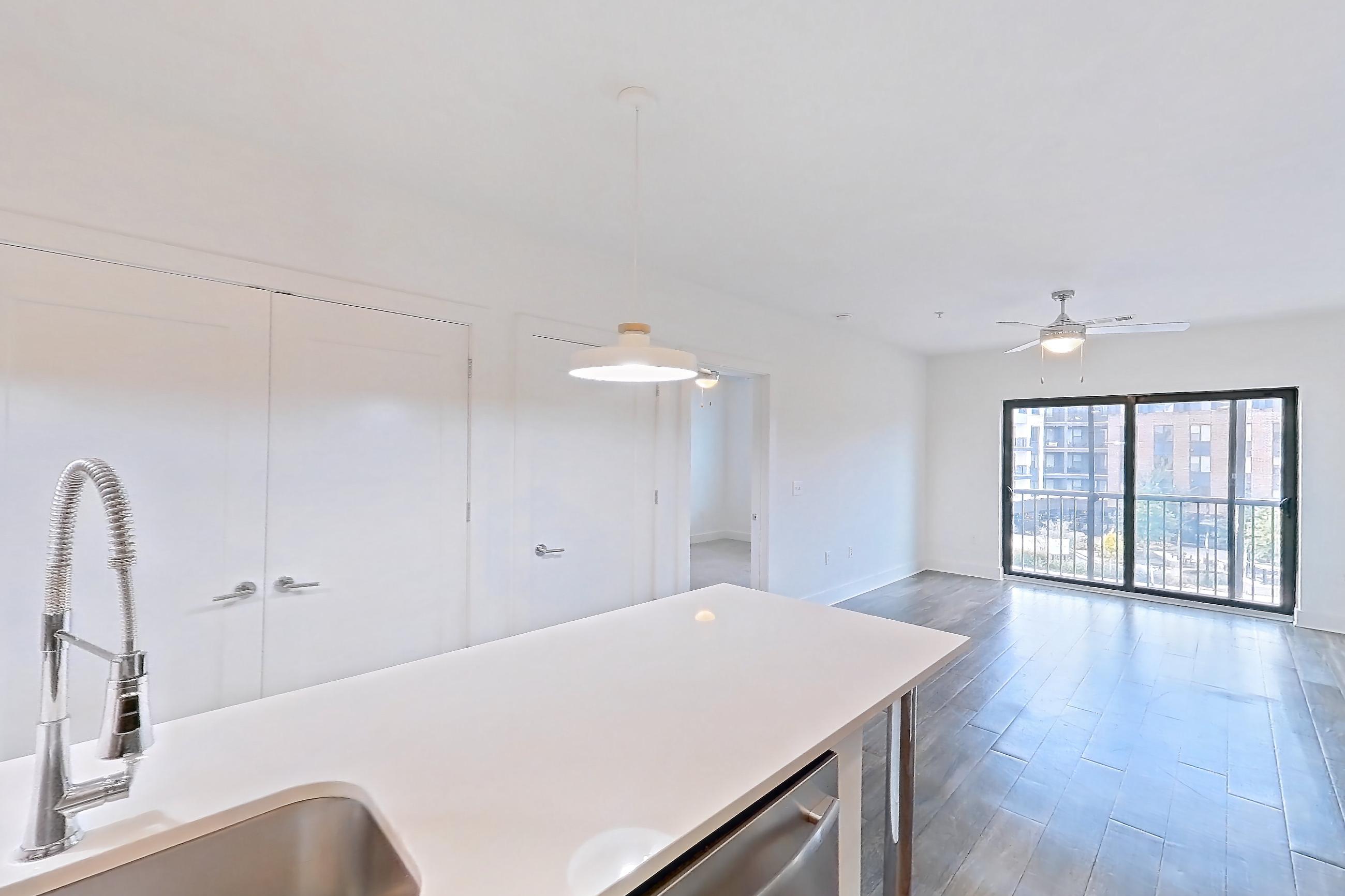 Kitchen with dark wood-finish flooring, dishwasher, electric range, kitchen island, light countertops, light stone countertops, microwave, oven/range, refrigerator, stainless steel appliances, and water & ice dispenser, Apartment 445 at Cortland at the Battery
