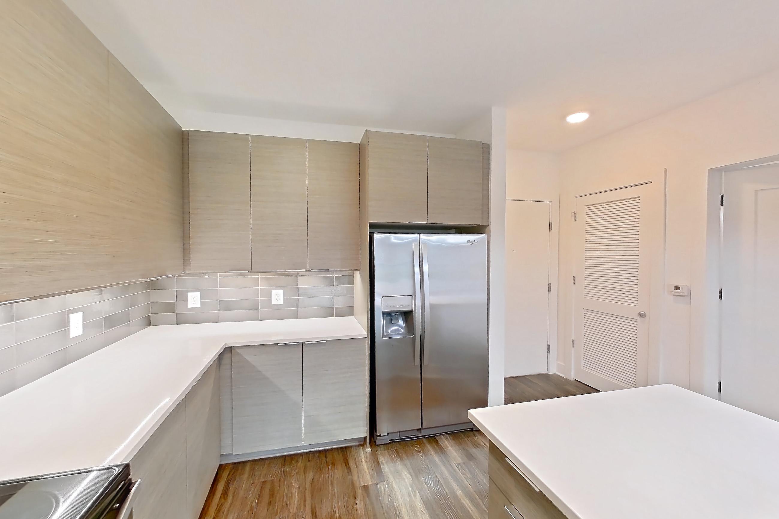 Kitchen with dark wood-finish flooring, dishwasher, electric range, kitchen island, light countertops, light stone countertops, microwave, oven/range, refrigerator, stainless steel appliances, and water & ice dispenser, Apartment 445 at Cortland at the Battery