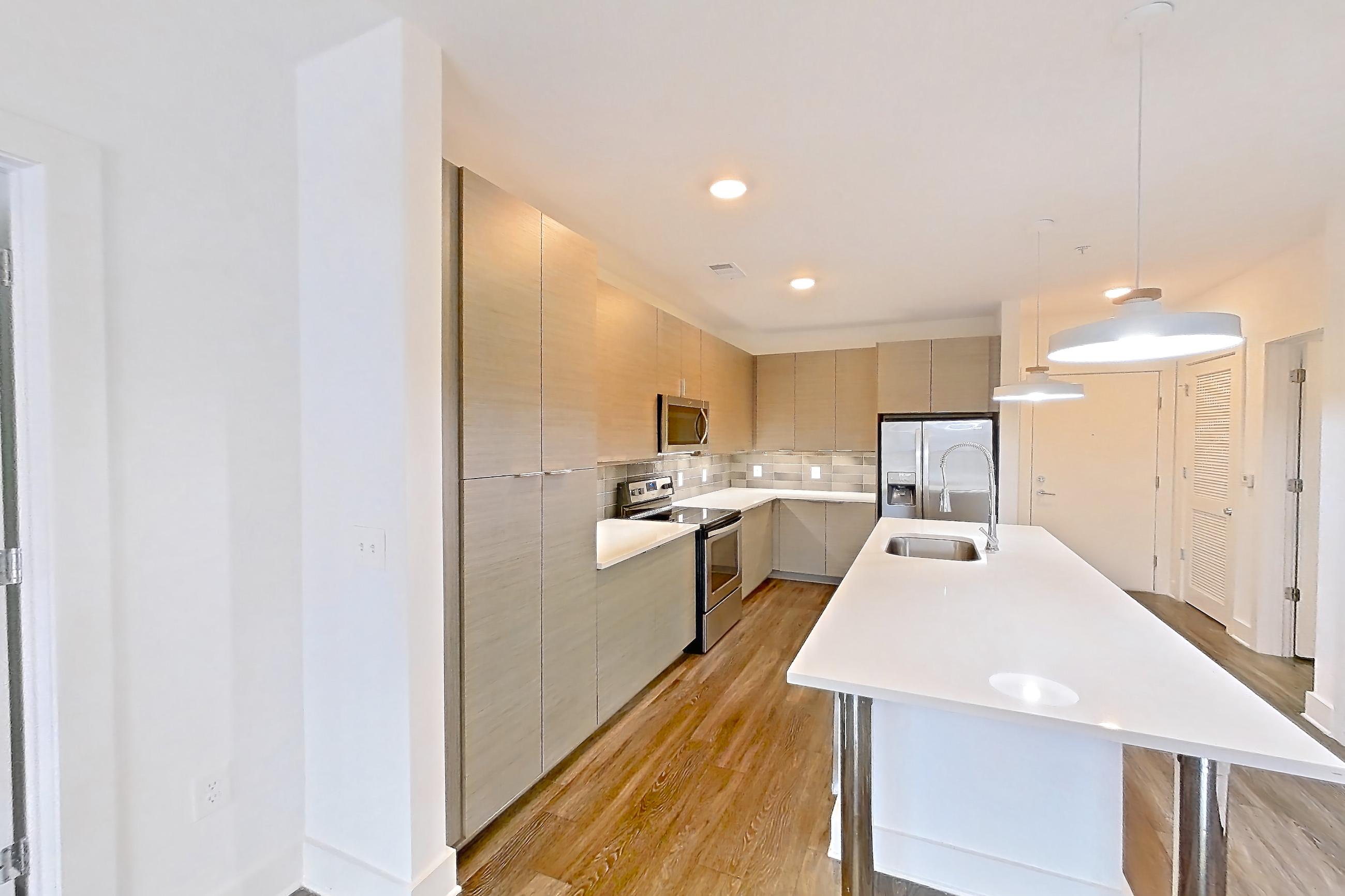 Living room with dark wood-finish flooring, electric range, kitchen island, light stone countertops, microwave, oven/range, refrigerator, stainless steel appliances, and water & ice dispenser, Apartment 445 at Cortland at the Battery