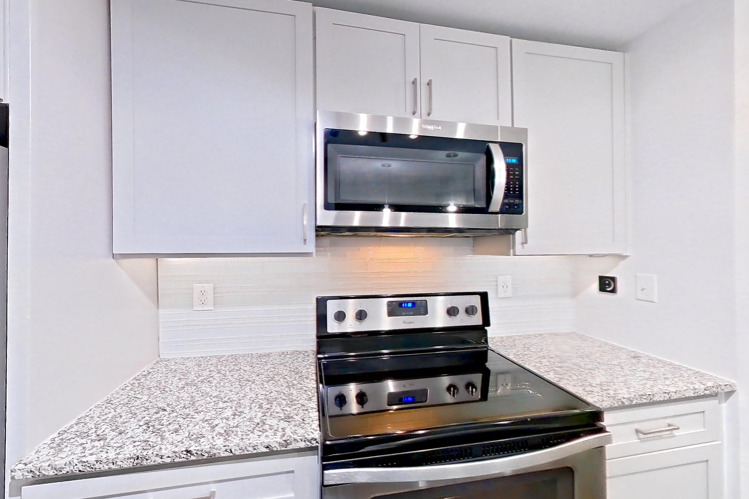 Kitchen with dark wood-finish flooring, dishwasher, electric range, light countertops, light stone countertops, microwave, oven/range, and stainless steel appliances, Apartment 2524 at Cortland Duluth