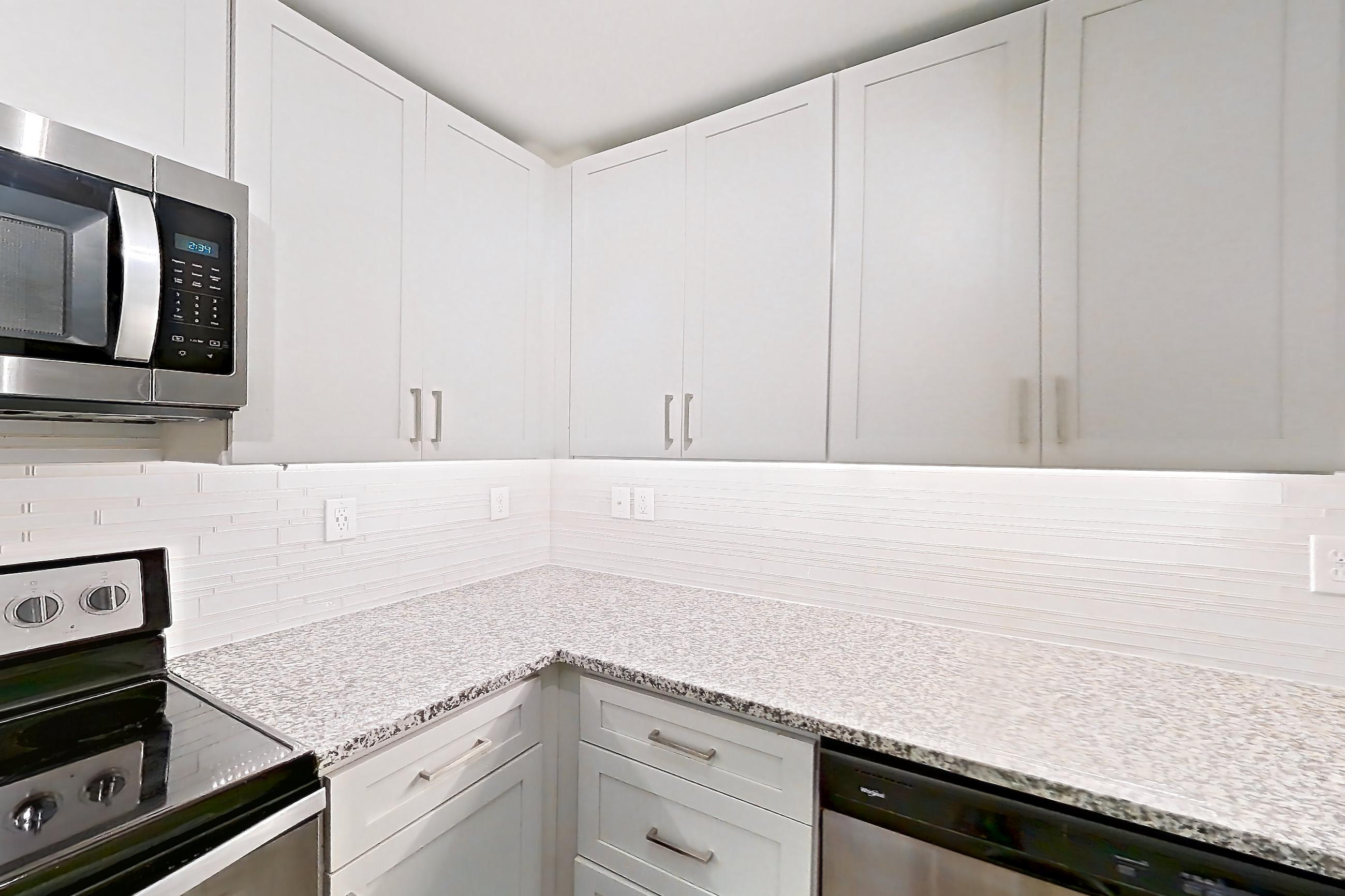 Kitchen with dishwasher, electric range, light countertops, light stone countertops, light wood-finish flooring, microwave, oven/range, refrigerator, and stainless steel appliances, Apartment 2924 at Cortland Duluth