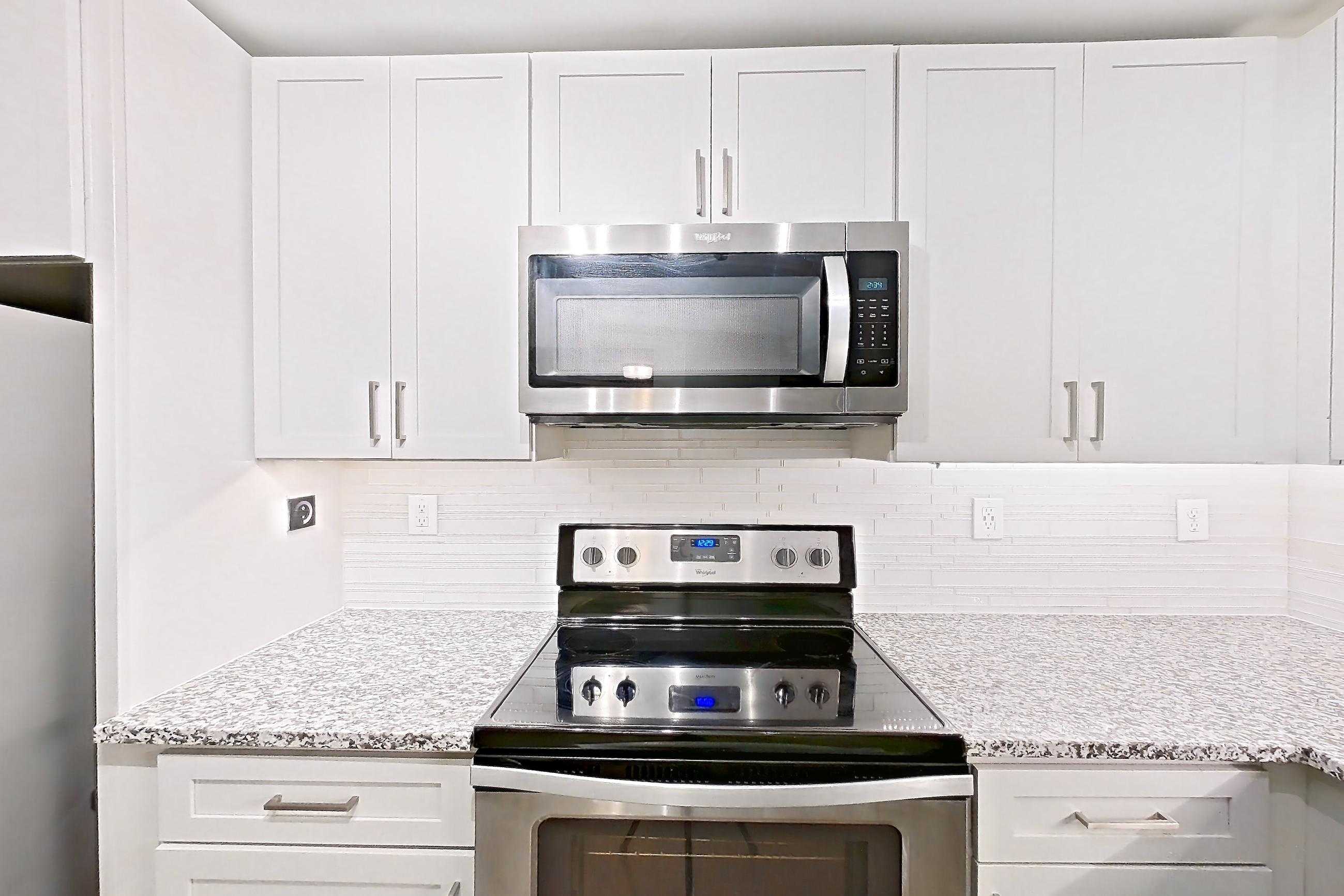 Kitchen with dishwasher, electric range, light countertops, light stone countertops, light wood-finish flooring, microwave, oven/range, refrigerator, and stainless steel appliances, Apartment 2924 at Cortland Duluth