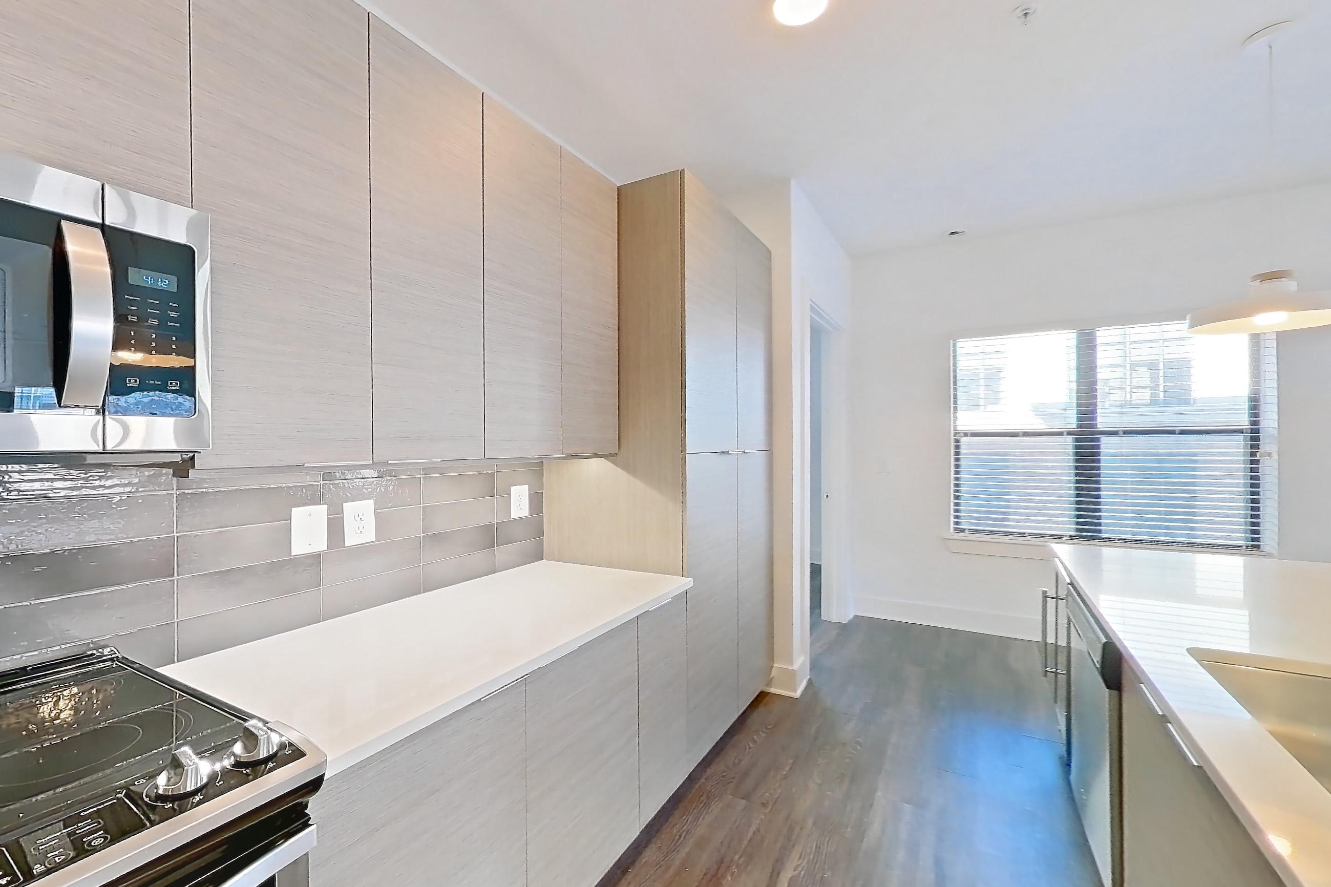 Kitchen with dark wood-finish flooring, electric range, kitchen island, light countertops, light stone countertops, microwave, oven/range, refrigerator, and stainless steel appliances, Apartment 432 at Cortland at the Battery