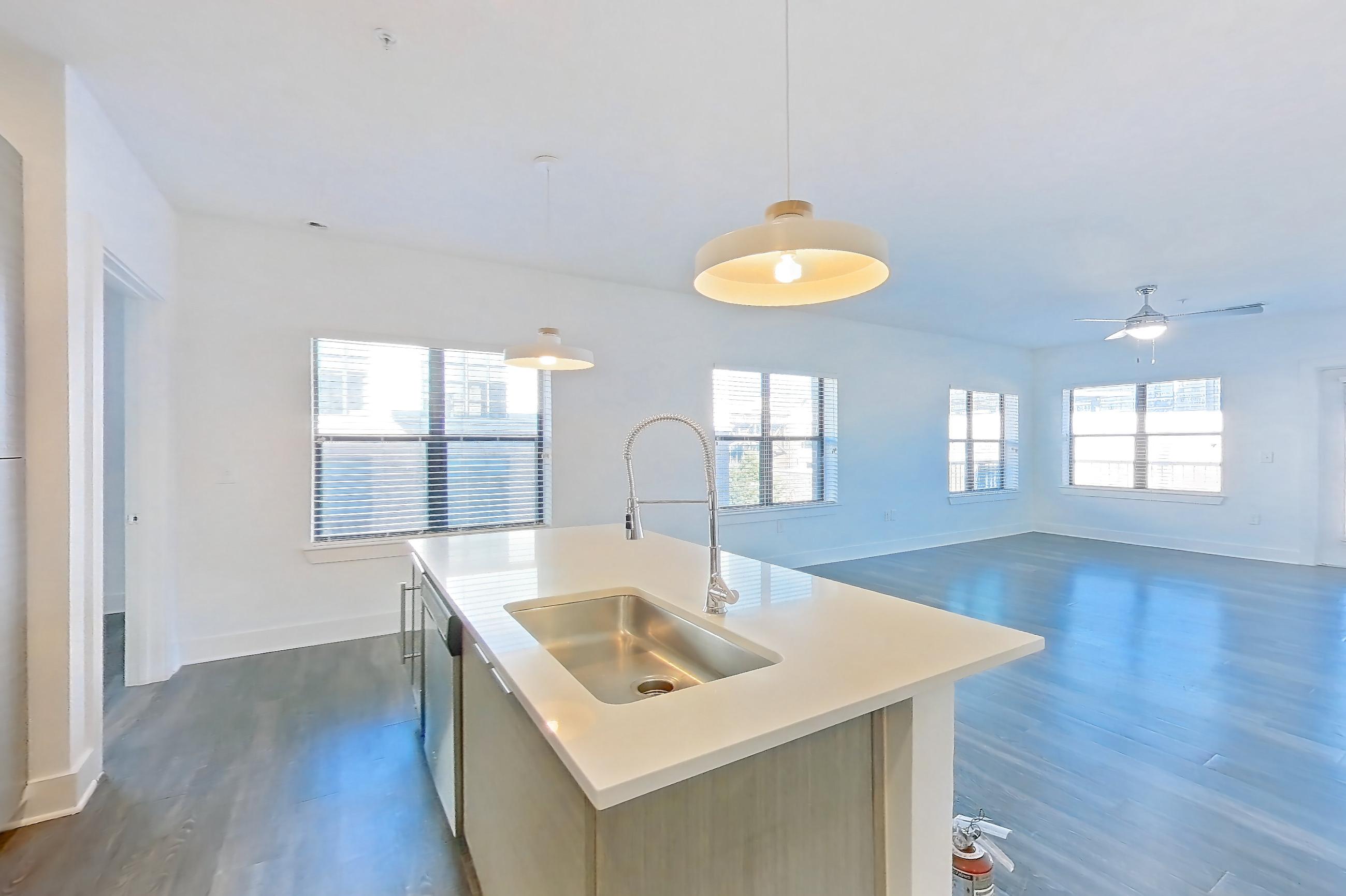 Kitchen with dark wood-finish flooring, electric range, kitchen island, light countertops, light stone countertops, microwave, oven/range, refrigerator, and stainless steel appliances, Apartment 432 at Cortland at the Battery