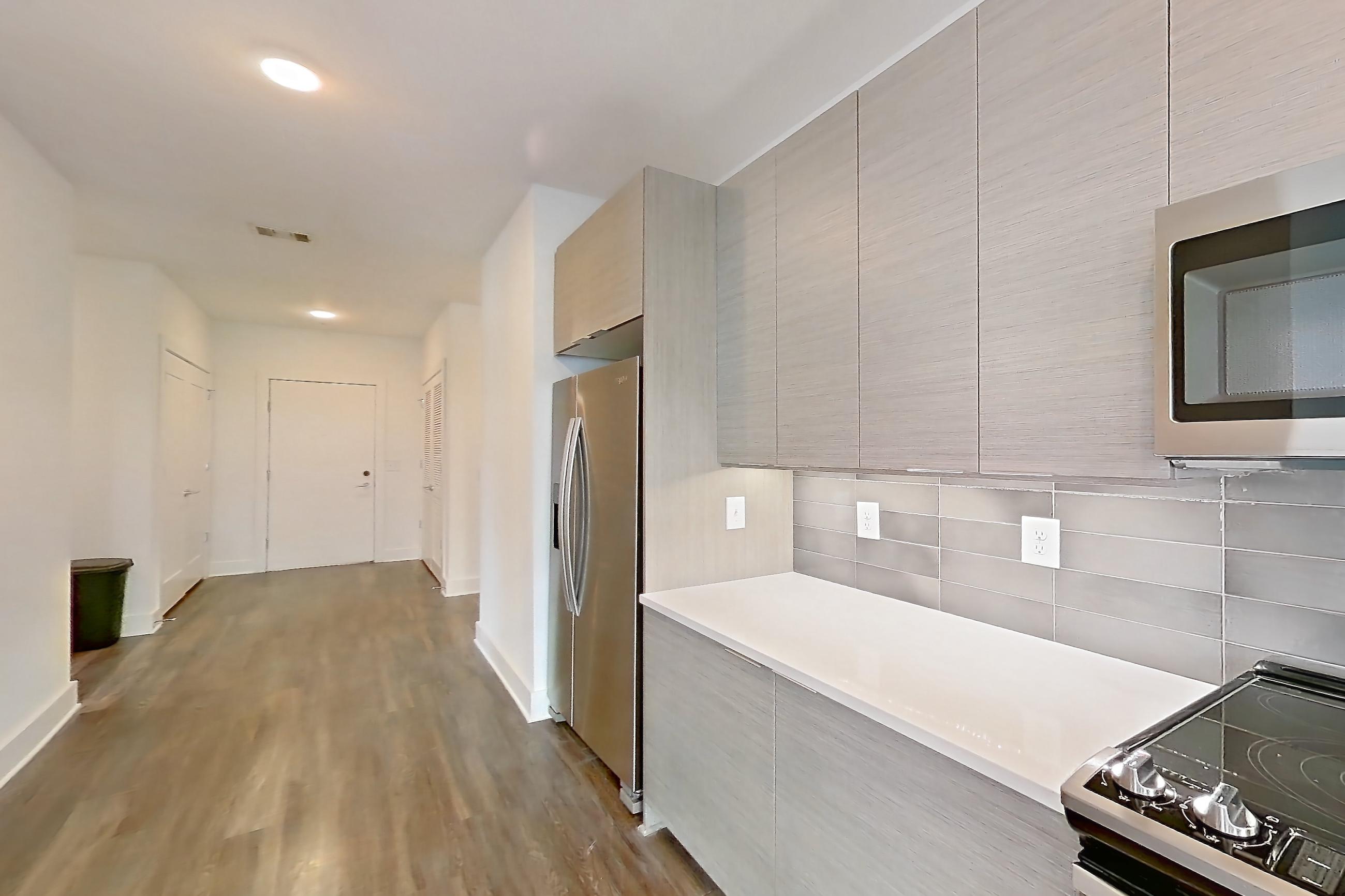 Kitchen with dark wood-finish flooring, electric range, kitchen island, light countertops, light stone countertops, microwave, oven/range, refrigerator, and stainless steel appliances, Apartment 432 at Cortland at the Battery