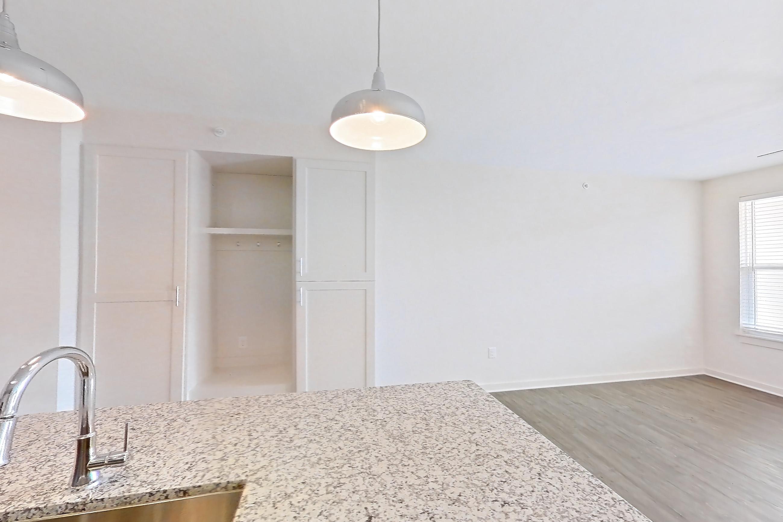 Kitchen with dark wood-finish flooring, dishwasher, electric range, kitchen island, light countertops, light stone countertops, microwave, oven/range, refrigerator, stainless steel appliances, and water & ice dispenser, Apartment 2-108 at Cortland Wren Northlake