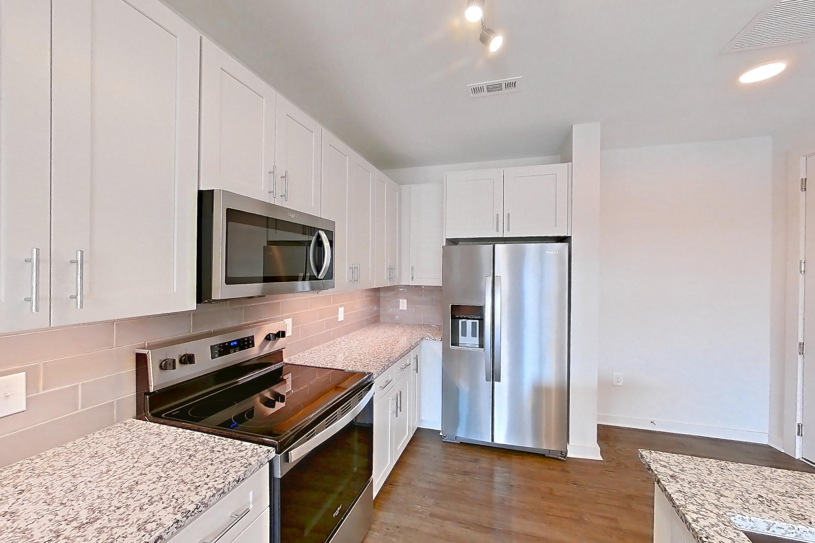 Kitchen with dark wood-finish flooring, dishwasher, electric range, kitchen island, light countertops, light stone countertops, microwave, oven/range, refrigerator, stainless steel appliances, and water & ice dispenser, Apartment 2-108 at Cortland Wren Northlake