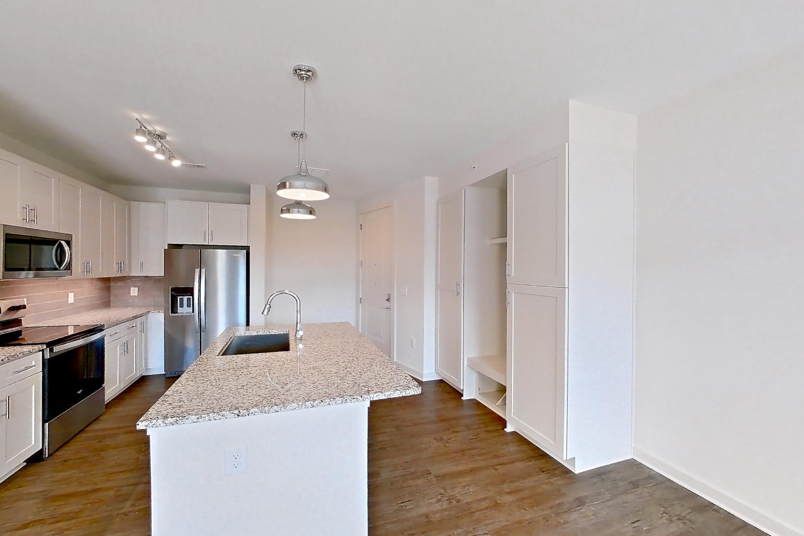 Living space with dark wood-finish flooring, electric range, kitchen island, light countertops, light stone countertops, oven/range, refrigerator, stainless steel appliances, and water & ice dispenser, Apartment 2-108 at Cortland Wren Northlake