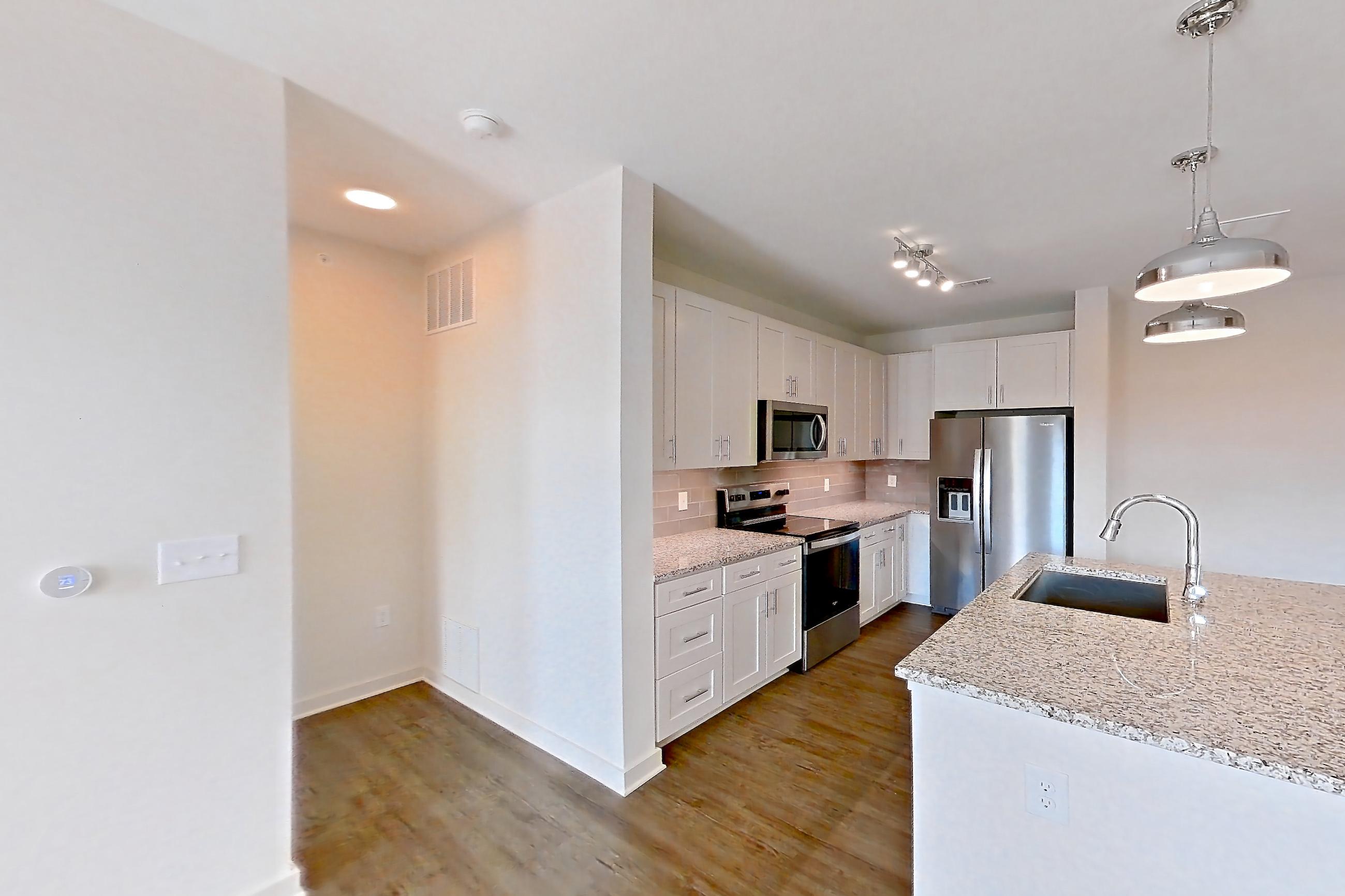 Living space with dark wood-finish flooring, electric range, kitchen island, light countertops, light stone countertops, oven/range, refrigerator, stainless steel appliances, and water & ice dispenser, Apartment 2-108 at Cortland Wren Northlake