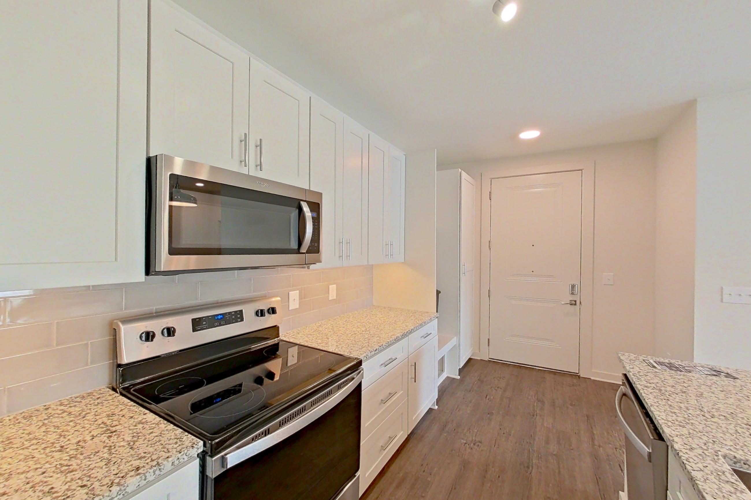 Kitchen with black appliances, dark wood-finish flooring, electric range, kitchen island, light countertops, light stone countertops, microwave, oven/range, refrigerator, stainless steel appliances, and water & ice dispenser, Apartment 3-209 at Cortland Wren Northlake