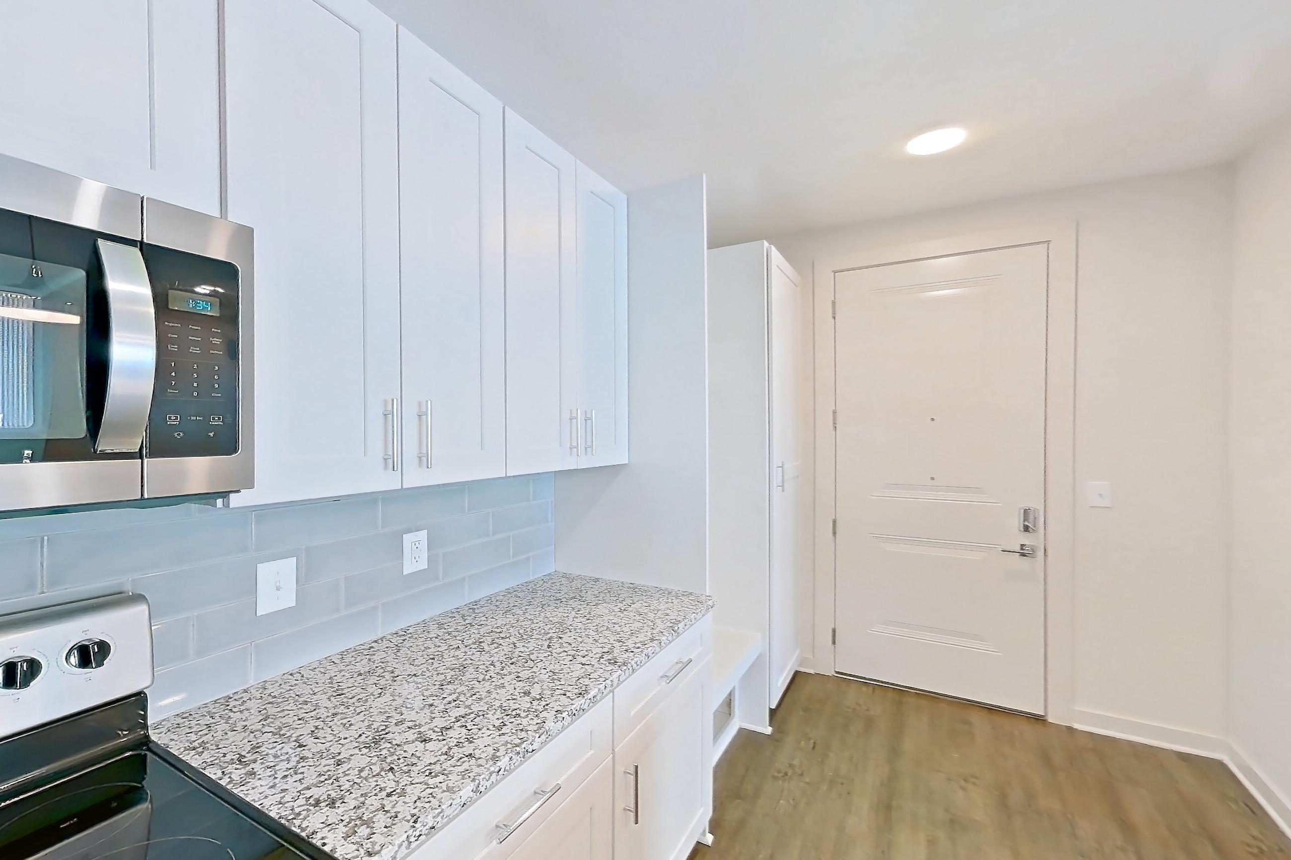 Kitchen with dark wood-finish flooring, dishwasher, electric range, kitchen island, light stone countertops, oven/range, and stainless steel appliances, Apartment 5-209 at Cortland Wren Northlake