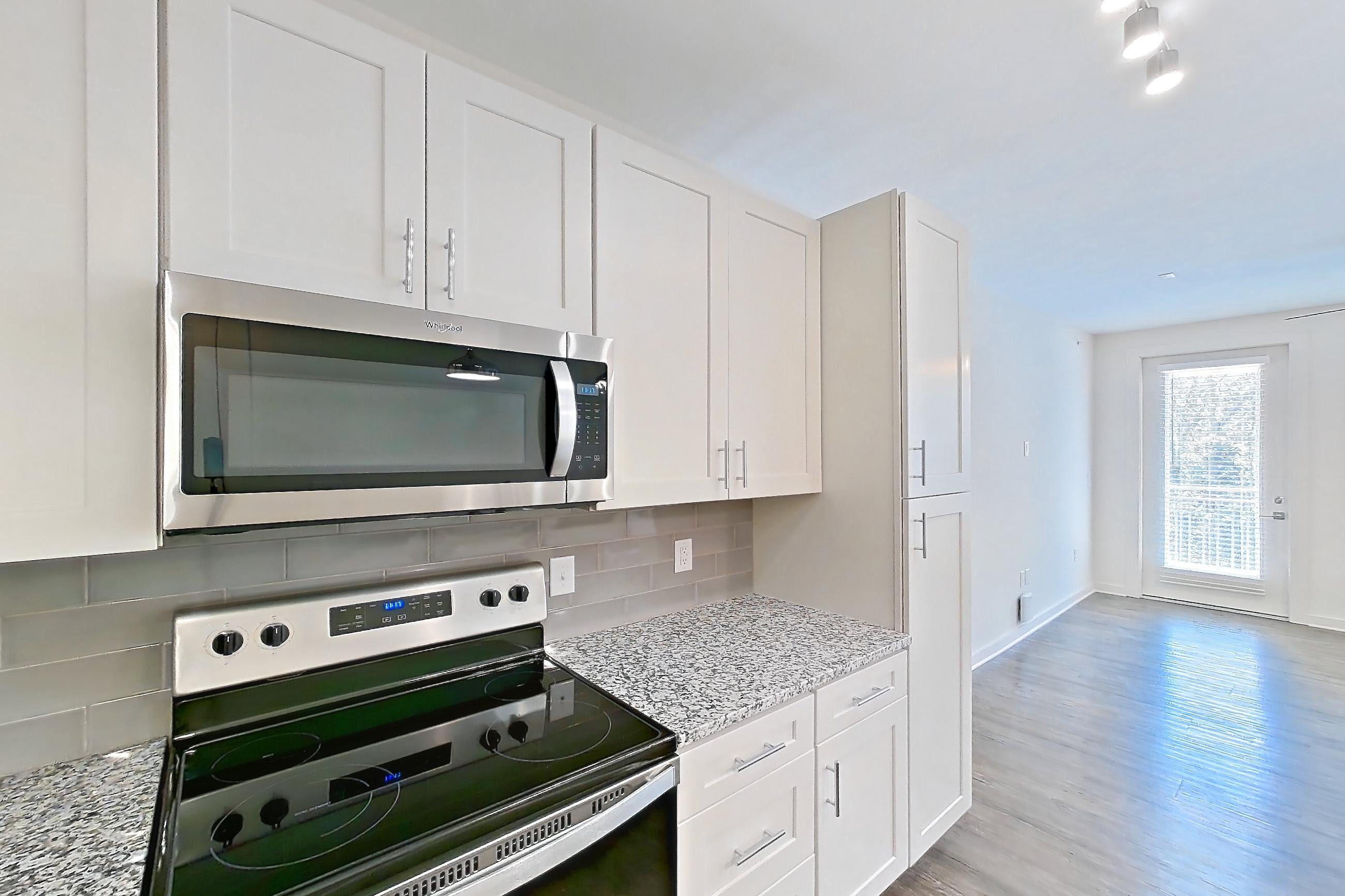 Kitchen with dark wood-finish flooring, electric range, kitchen island, light countertops, light stone countertops, microwave, oven/range, refrigerator, and stainless steel appliances, Apartment 5-310 at Cortland Wren Northlake
