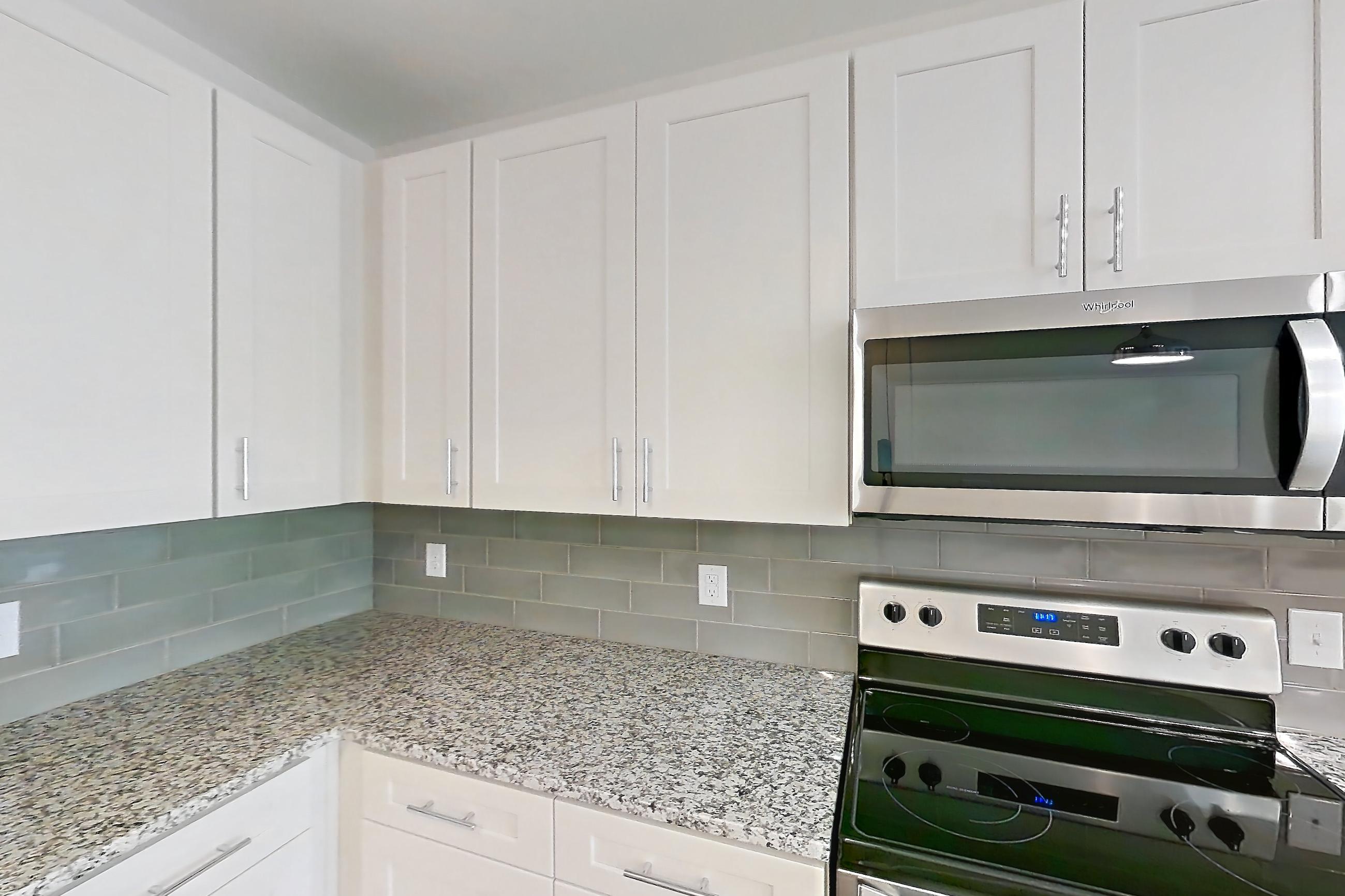 Kitchen with dark wood-finish flooring, electric range, kitchen island, light countertops, light stone countertops, microwave, oven/range, refrigerator, and stainless steel appliances, Apartment 5-310 at Cortland Wren Northlake