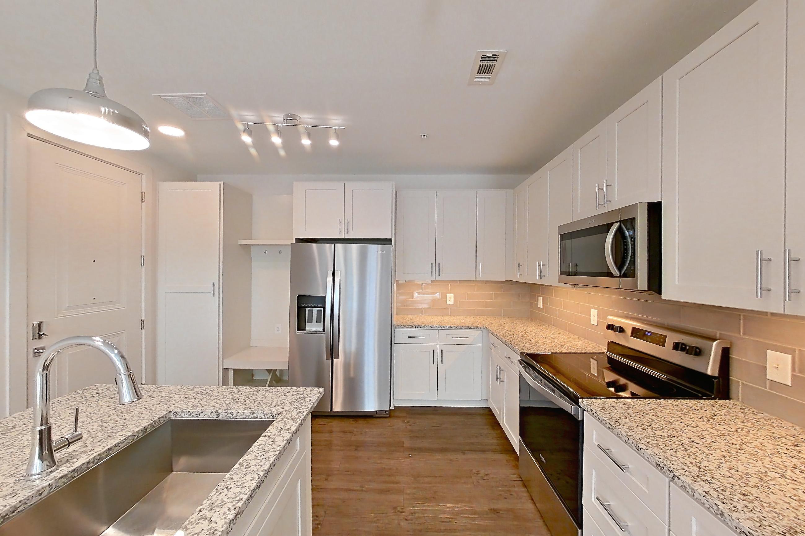 Kitchen with dark wood-finish flooring, electric range, light countertops, light stone countertops, oven/range, refrigerator, stainless steel appliances, and water & ice dispenser, Apartment 6-210 at Cortland Wren Northlake