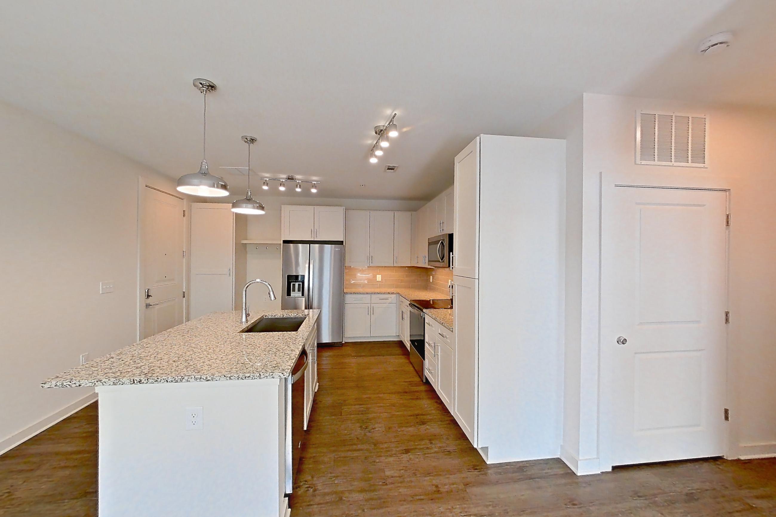 Living space with dark wood-finish flooring, electric range, kitchen island, light countertops, light stone countertops, microwave, oven/range, refrigerator, stainless steel appliances, and water & ice dispenser, Apartment 6-210 at Cortland Wren Northlake