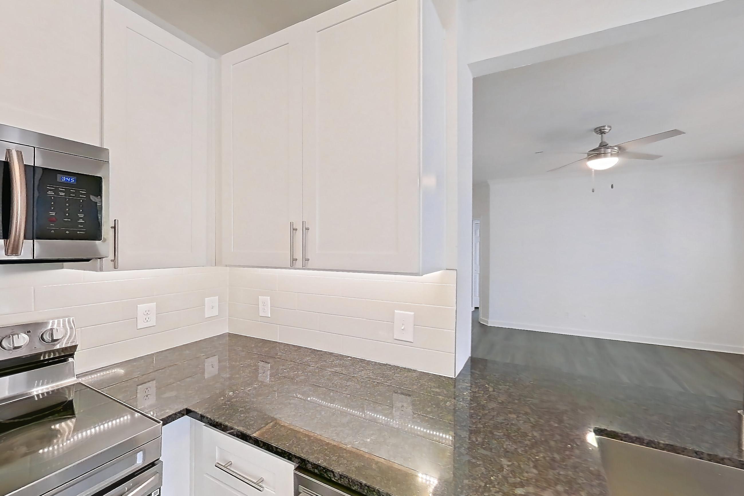 Kitchen with dark stone countertops, dark wood-finish flooring, dishwasher, electric range, light countertops, microwave, oven/range, refrigerator, and stainless steel appliances, Apartment 02432 at Cortland West Plano