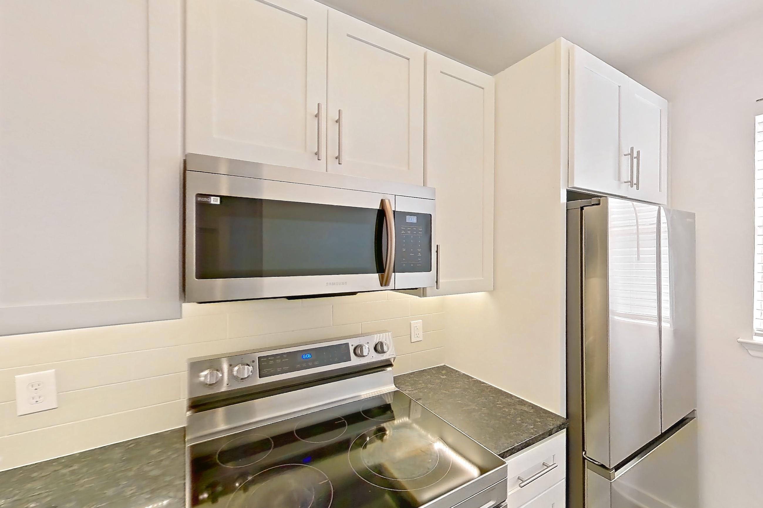 Kitchen with dark stone countertops, dark wood-finish flooring, dishwasher, electric range, light countertops, microwave, oven/range, and stainless steel appliances, Apartment 02831 at Cortland West Plano