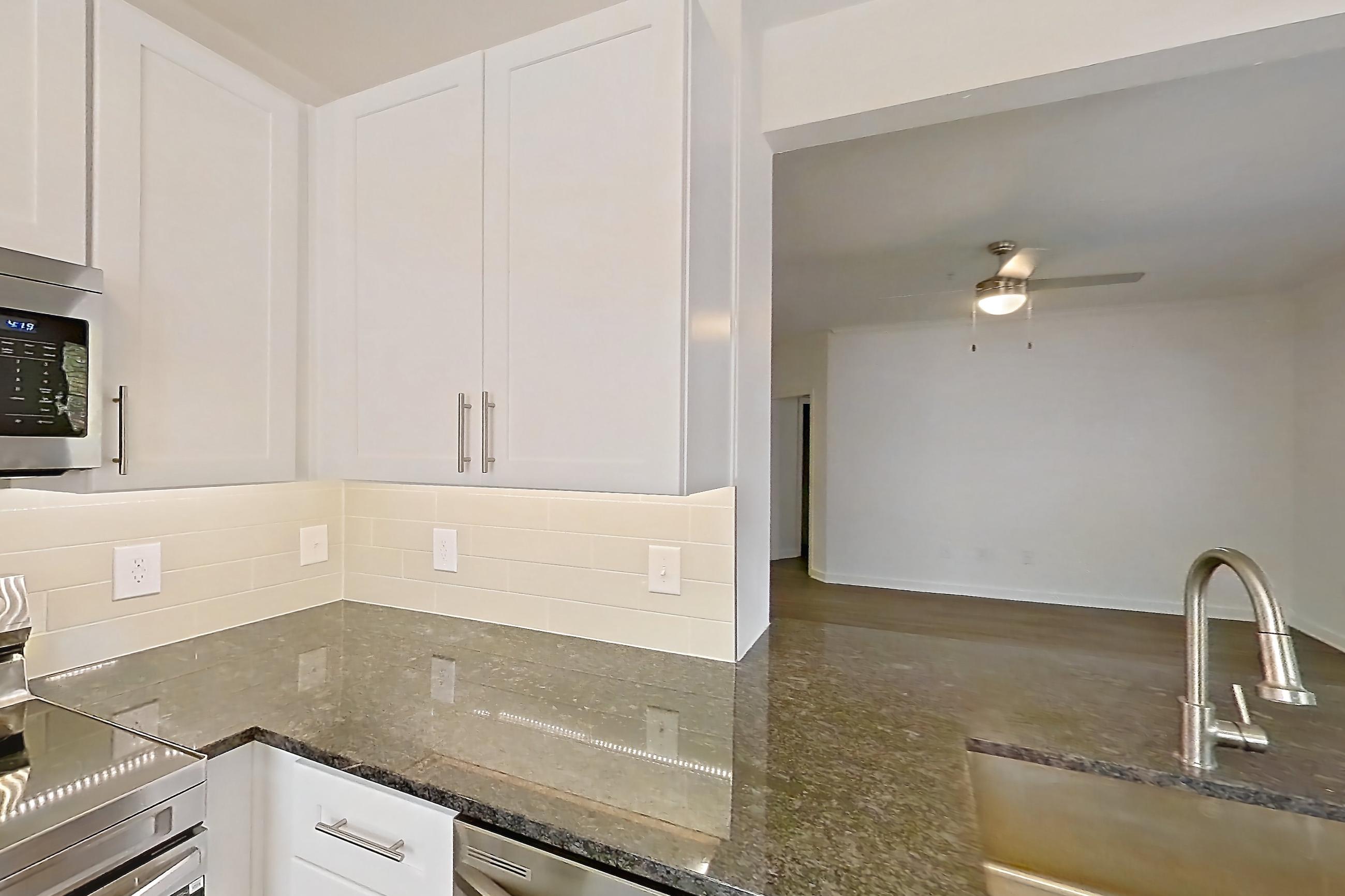 Kitchen with dark stone countertops, dark wood-finish flooring, dishwasher, electric range, light countertops, microwave, oven/range, refrigerator, stainless steel appliances, and white appliances, Apartment 03025 at Cortland West Plano