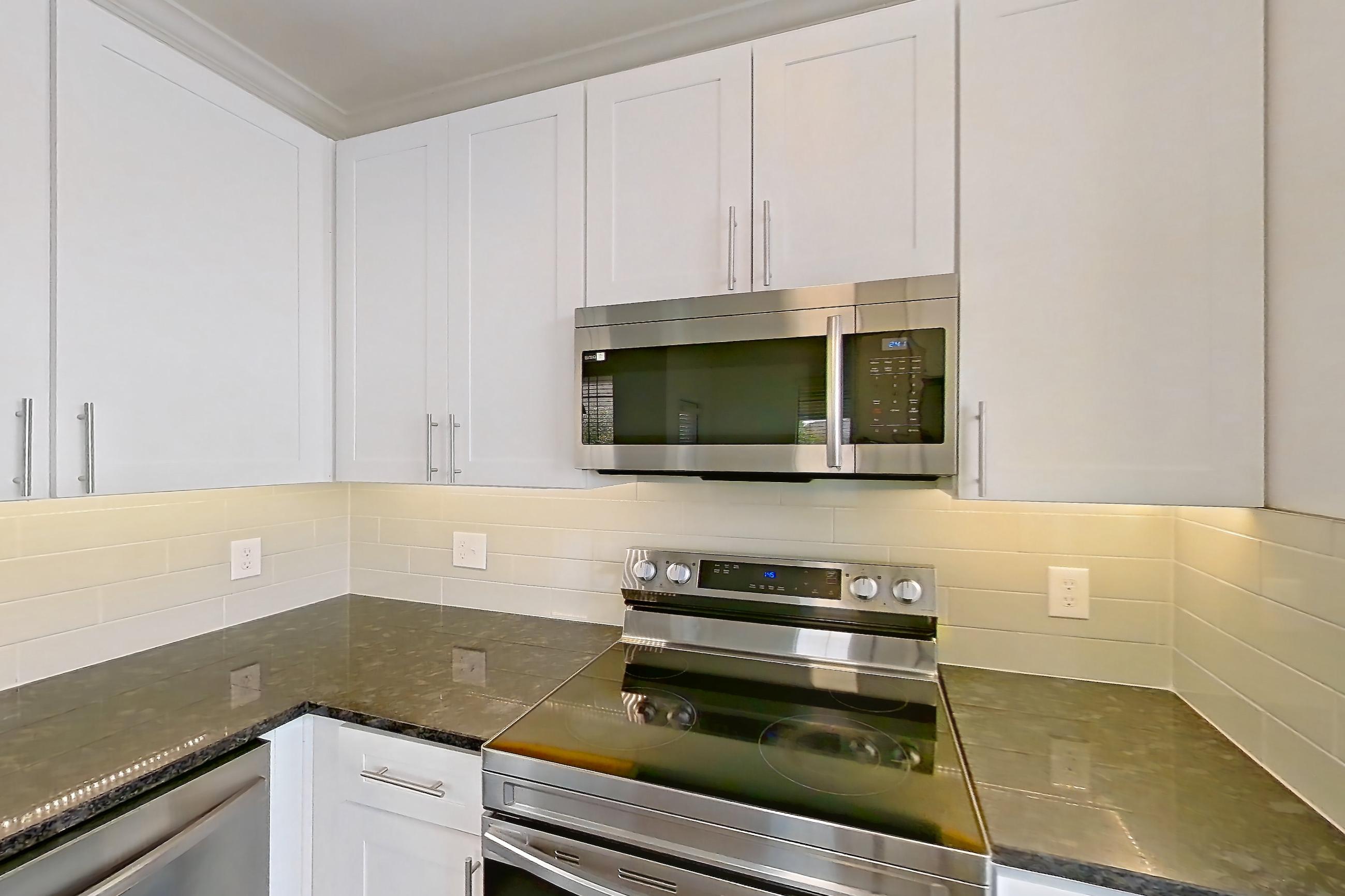 Kitchen with dark stone countertops, dark wood-finish flooring, dishwasher, electric range, light countertops, microwave, oven/range, refrigerator, and stainless steel appliances, Apartment 06301 at Cortland West Plano