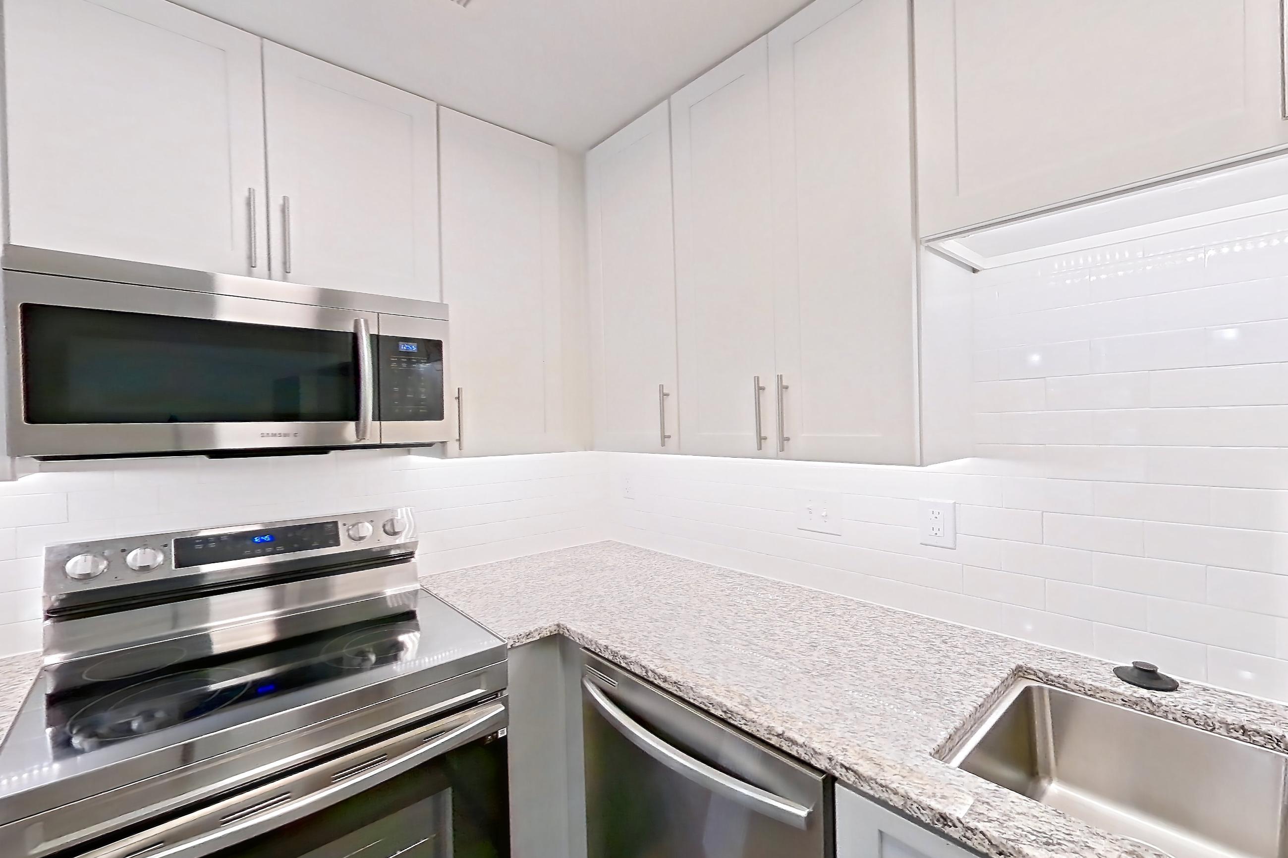 Kitchen with dark wood-finish flooring, dishwasher, electric range, light countertops, light stone countertops, microwave, oven/range, refrigerator, and stainless steel appliances, Apartment 2057G at Cortland at the Village