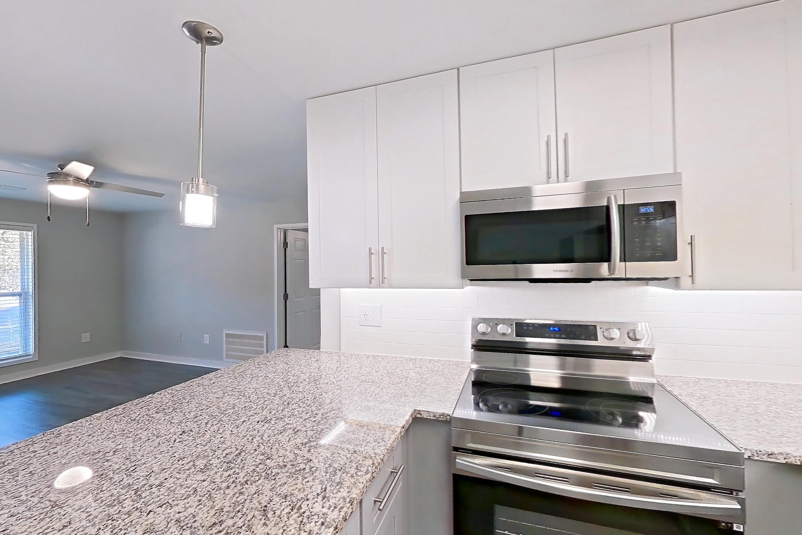 Kitchen with dark wood-finish flooring, dishwasher, electric range, light countertops, light stone countertops, microwave, oven/range, refrigerator, and stainless steel appliances, Apartment 2057G at Cortland at the Village