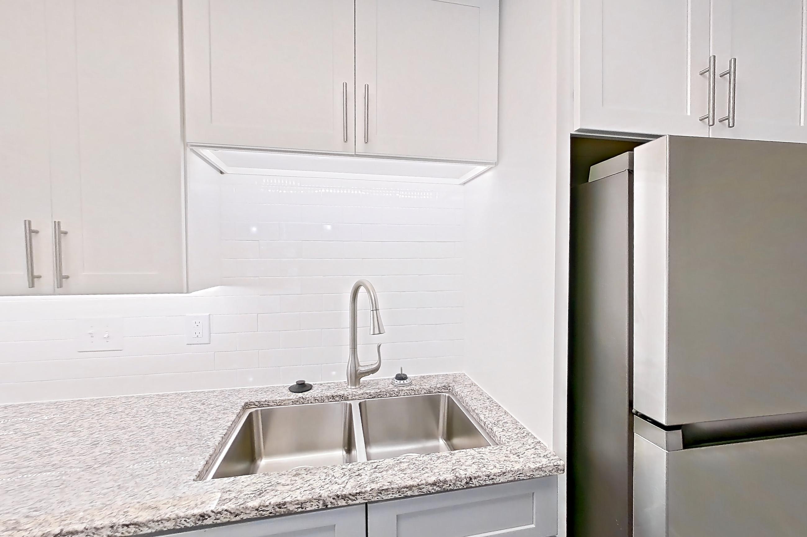 Kitchen with dark wood-finish flooring, dishwasher, electric range, light countertops, light stone countertops, microwave, oven/range, refrigerator, and stainless steel appliances, Apartment 2057G at Cortland at the Village