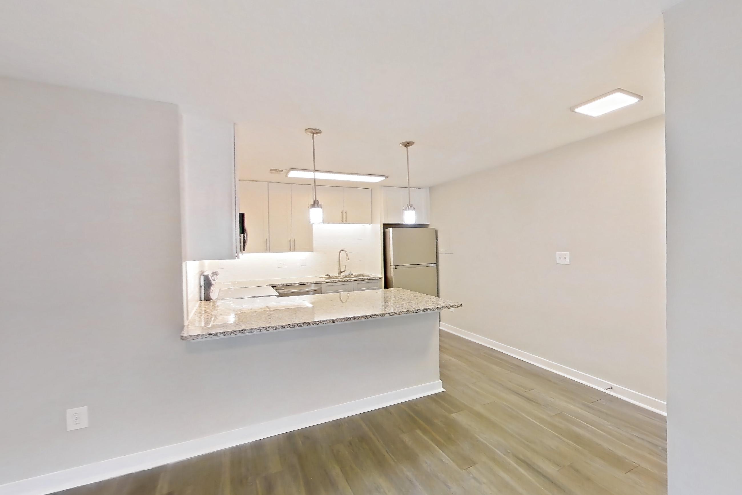 Living room with dark wood-finish flooring, dishwasher, refrigerator, stainless steel appliances, and white appliances, Apartment 2057G at Cortland at the Village