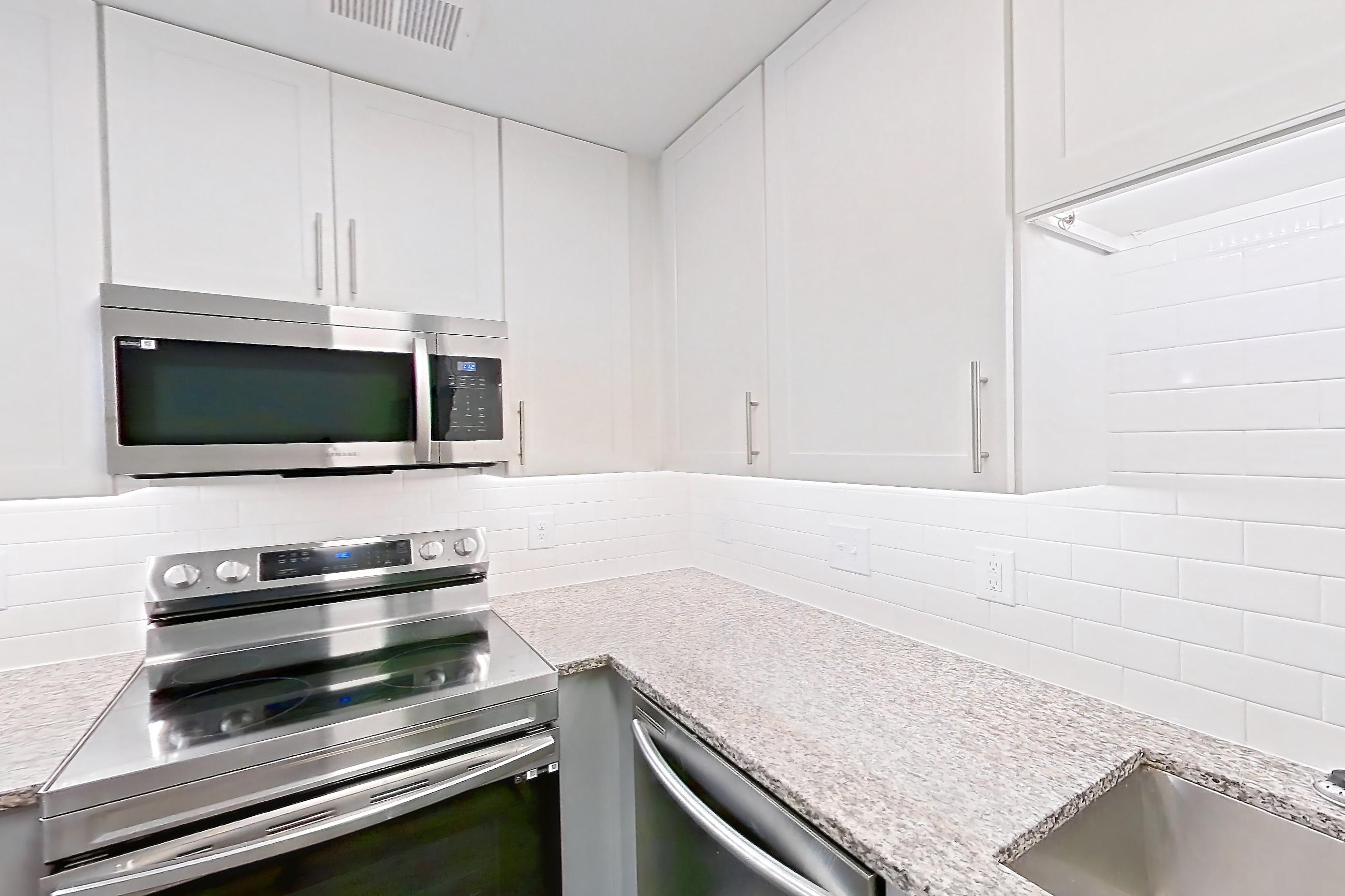 Kitchen with dark wood-finish flooring, dishwasher, electric range, light countertops, light stone countertops, microwave, oven/range, refrigerator, and stainless steel appliances, Apartment 2065Q at Cortland at the Village