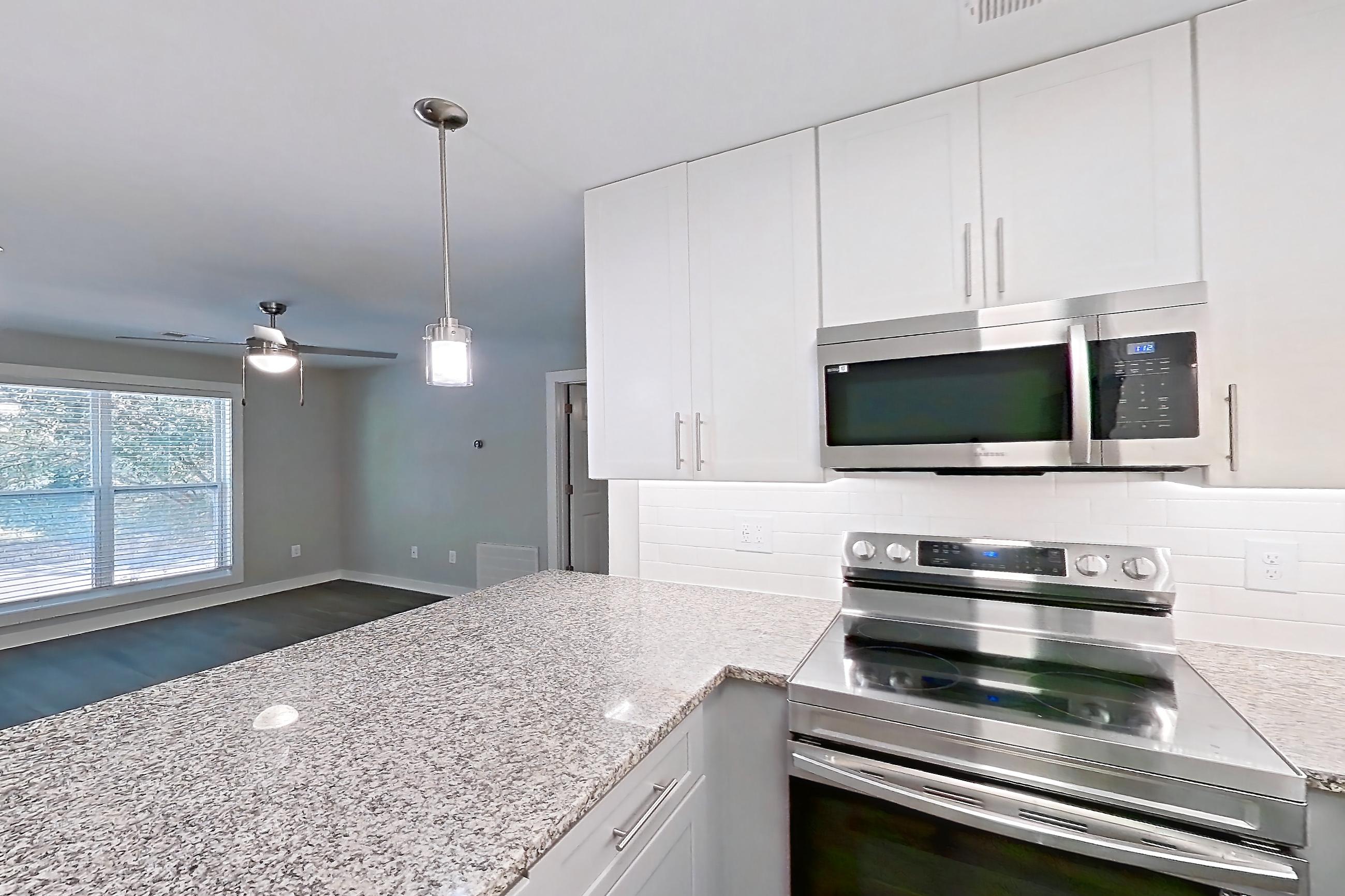 Kitchen with dark wood-finish flooring, dishwasher, electric range, light countertops, light stone countertops, microwave, oven/range, refrigerator, and stainless steel appliances, Apartment 2065Q at Cortland at the Village
