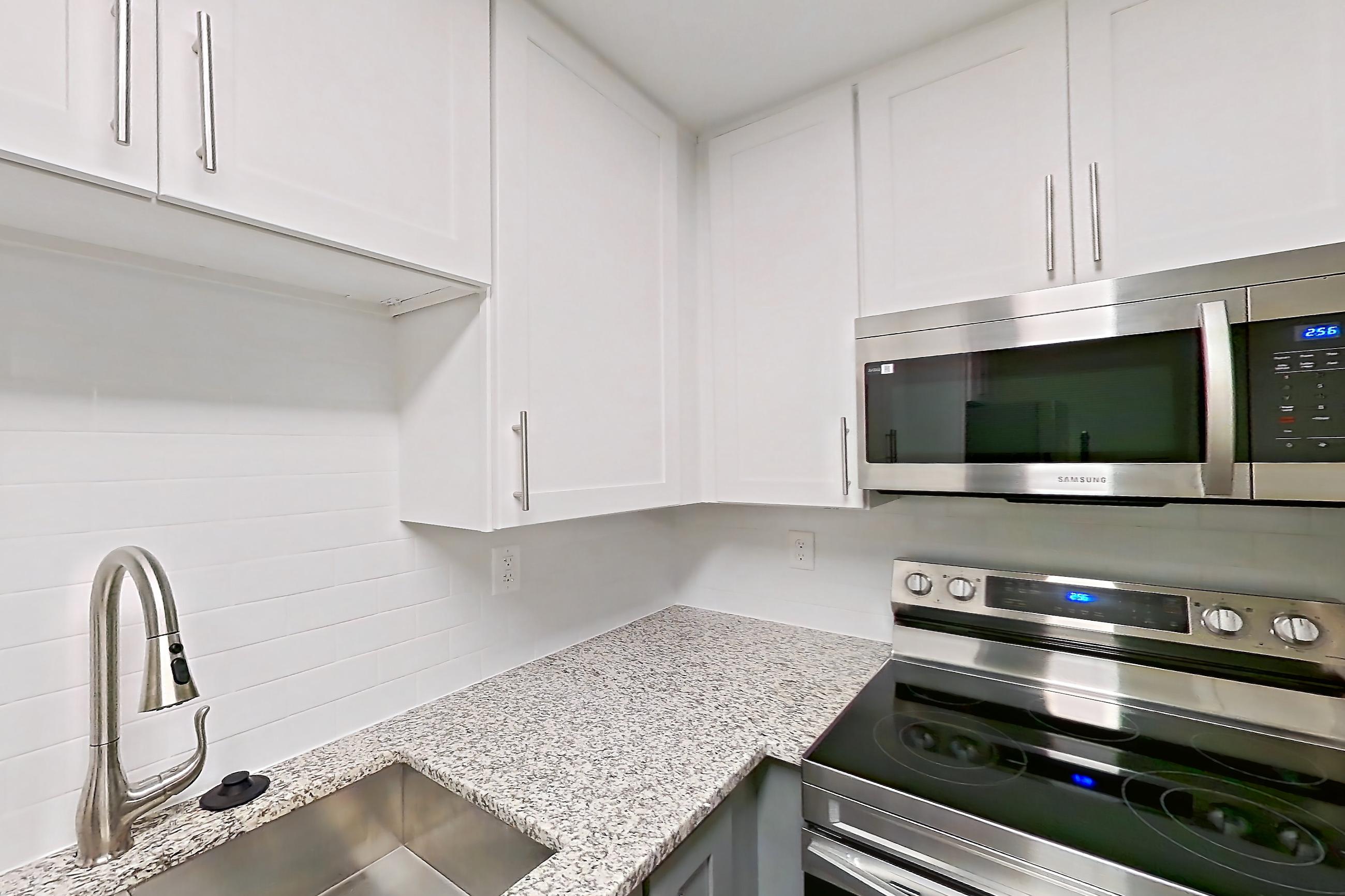 Kitchen with dishwasher, electric range, light countertops, light stone countertops, light wood-finish flooring, microwave, oven/range, refrigerator, and stainless steel appliances, Apartment 2083N at Cortland at the Village