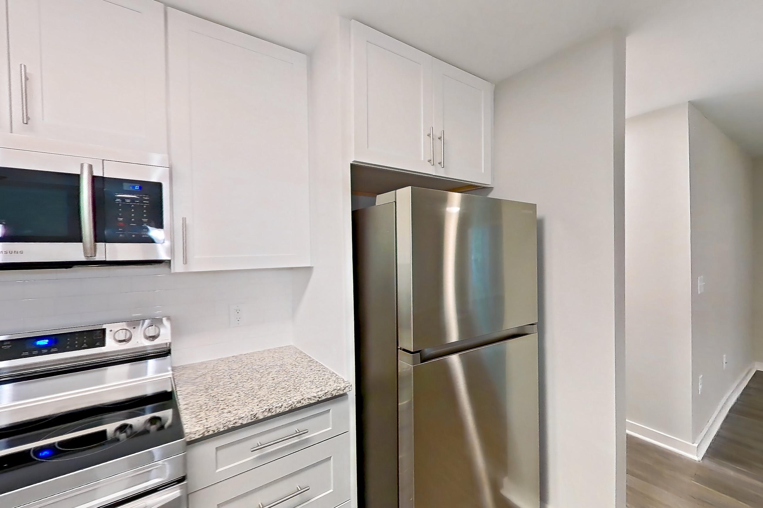 Kitchen with dark wood-finish flooring, dishwasher, electric range, light countertops, light stone countertops, light wood-finish flooring, microwave, oven/range, refrigerator, and stainless steel appliances, Apartment 2141O at Cortland at the Village