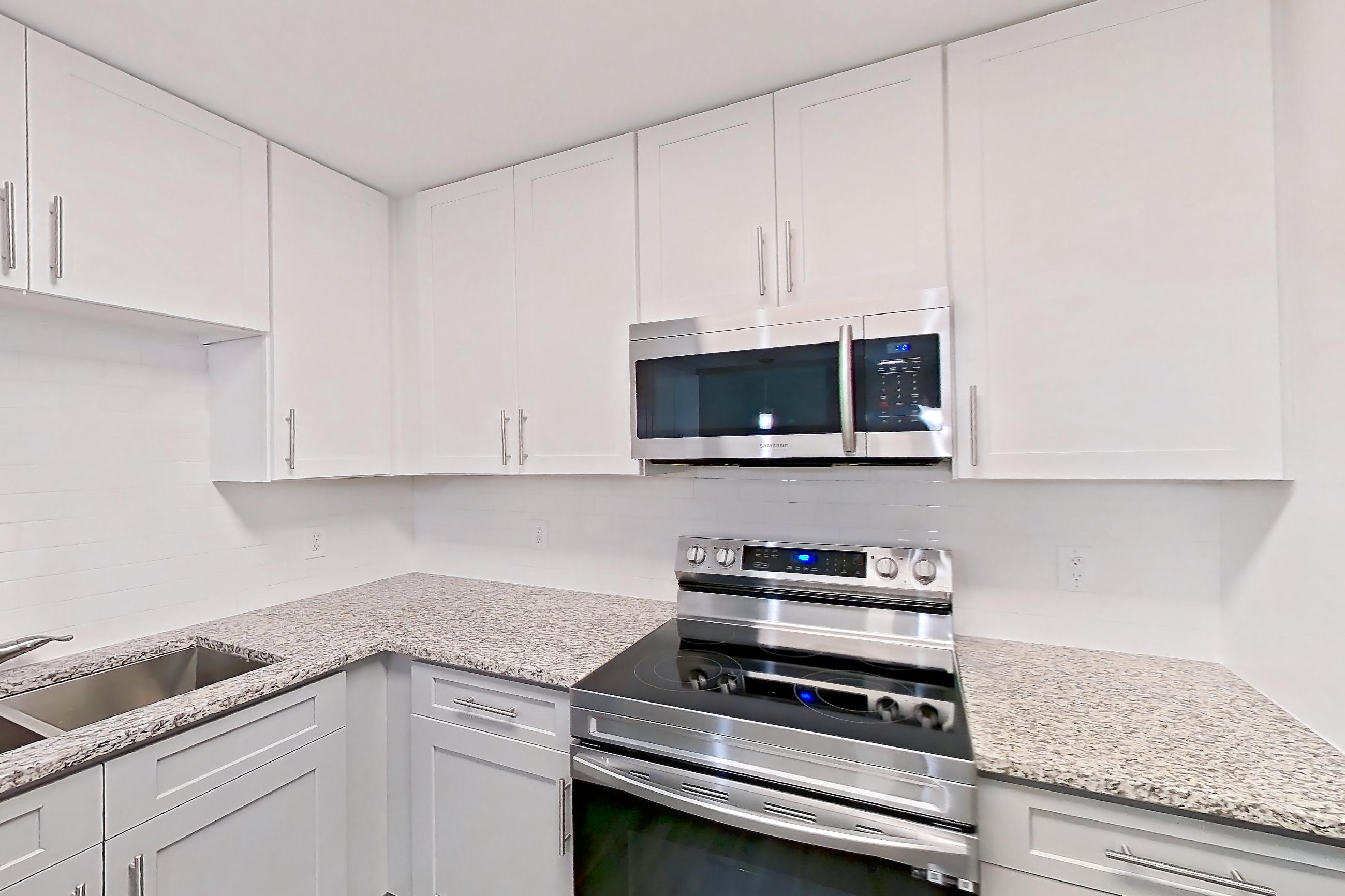 Kitchen with dark wood-finish flooring, dishwasher, electric range, light countertops, light stone countertops, light wood-finish flooring, microwave, oven/range, refrigerator, and stainless steel appliances, Apartment 2141O at Cortland at the Village