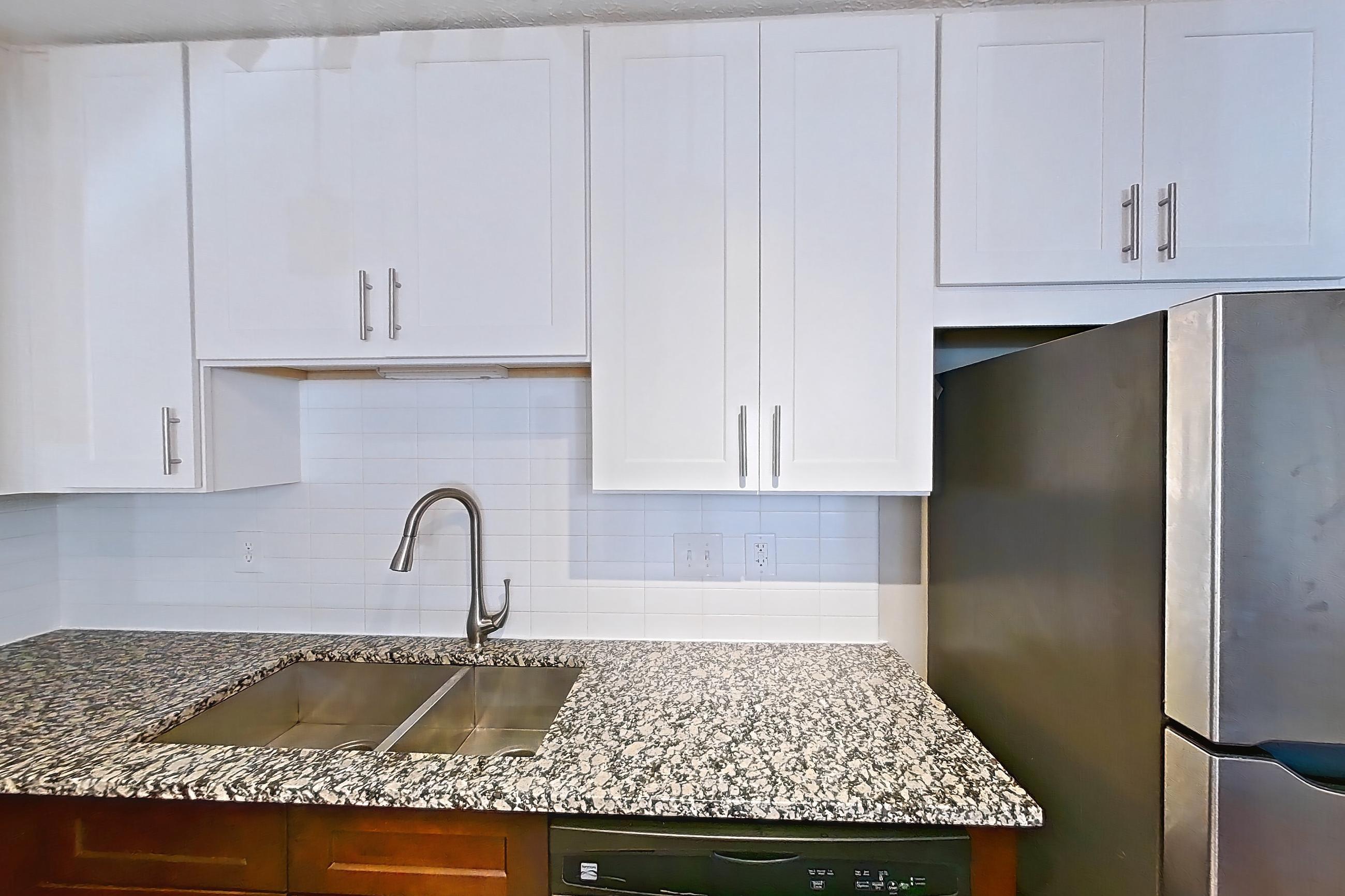 Kitchen with dark wood-finish flooring, dishwasher, electric range, light countertops, light stone countertops, light wood-finish flooring, microwave, oven/range, refrigerator, and stainless steel appliances, Apartment 2161D at Cortland at the Village